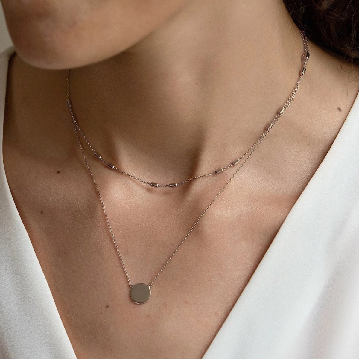 Sterling silver beaded choker layered with a round disc pendant necklace, shown on a model