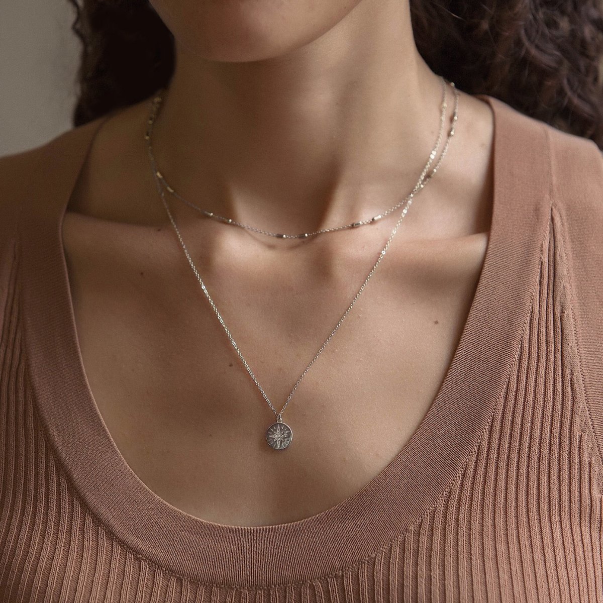 Sterling silver star disc necklace with a starburst pendant, shown on a model's neckline
