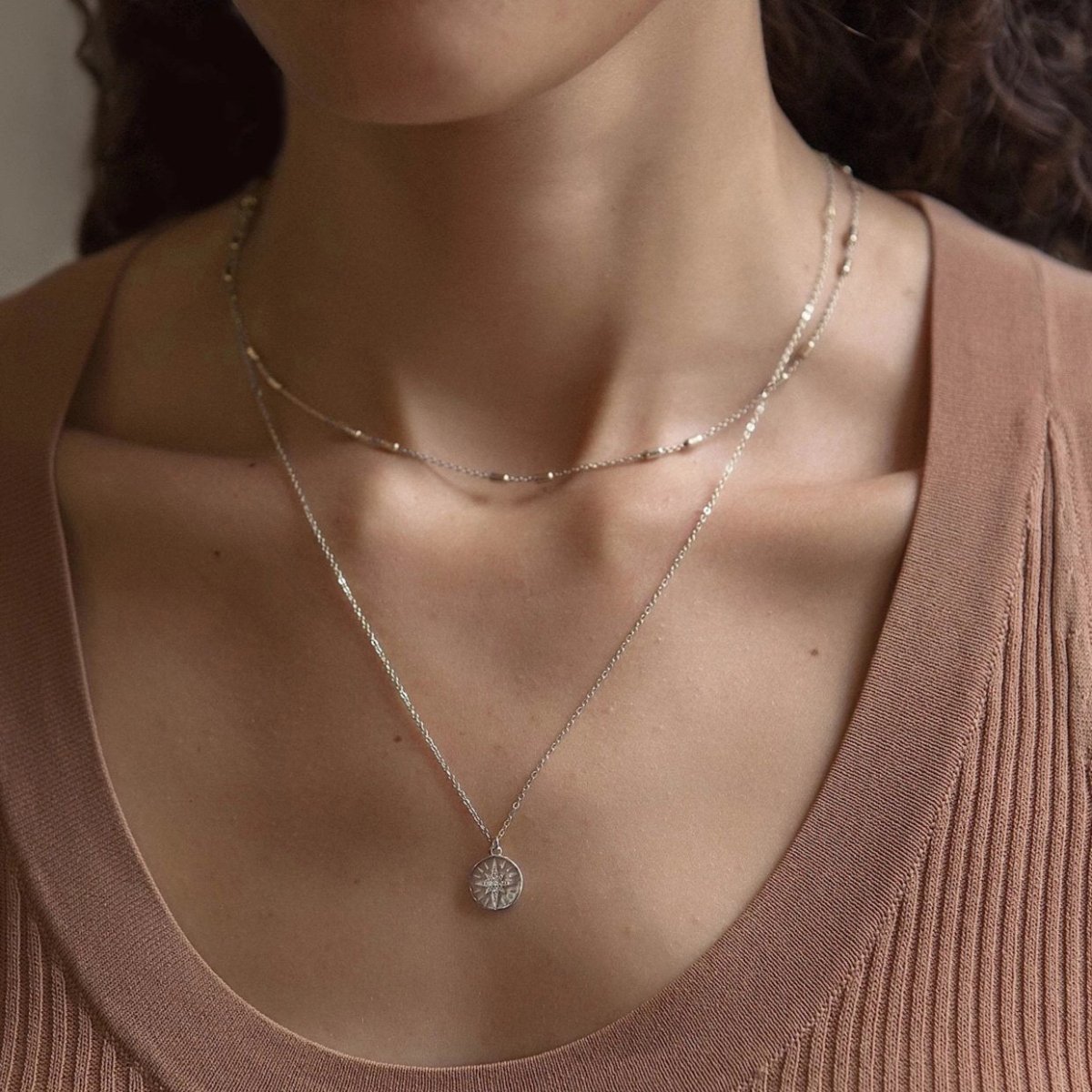 Sterling silver layered necklace duo with a starburst disc pendant, shown on a model's neckline