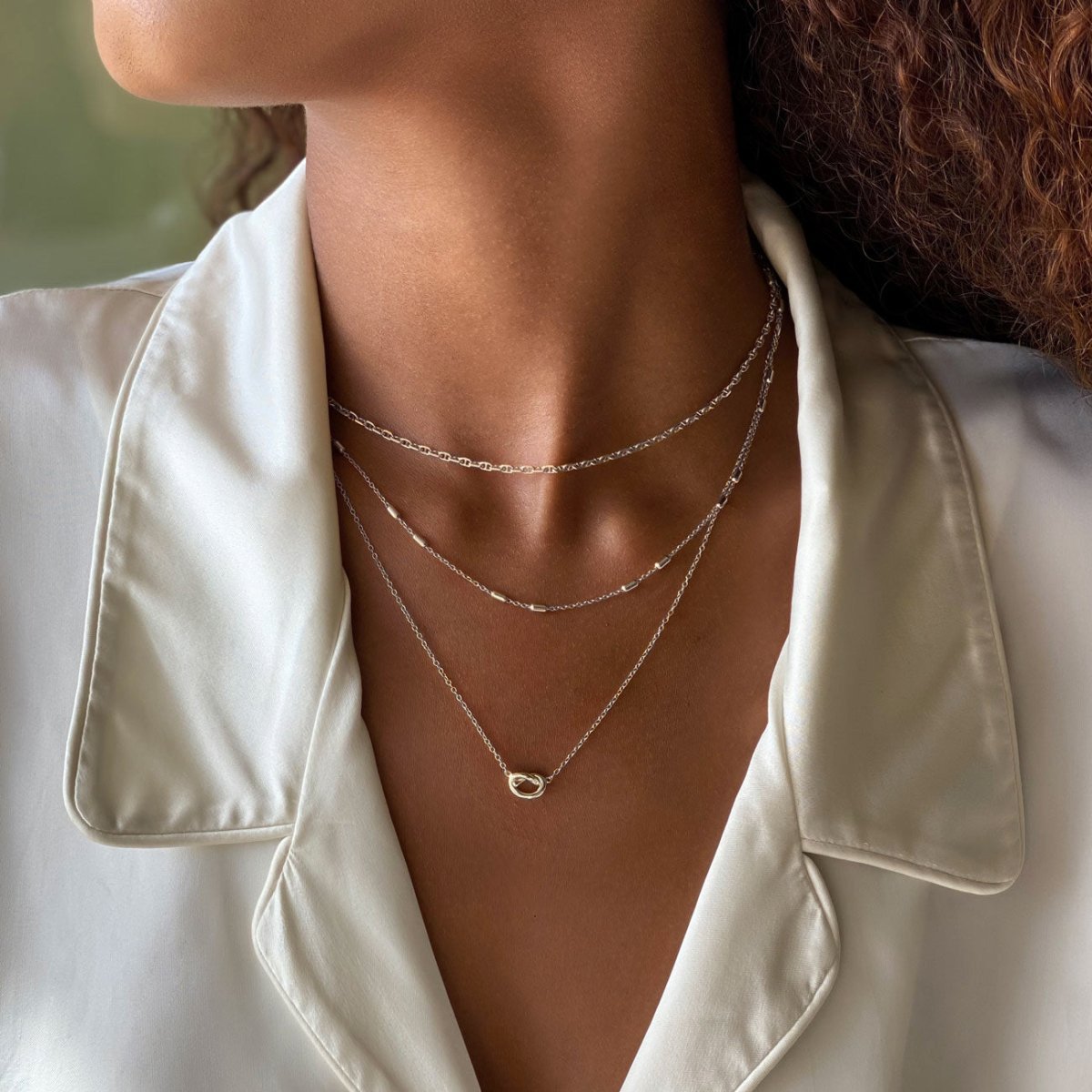 Sterling silver layered chains shown on a model's neckline with a small interlocking ring detail