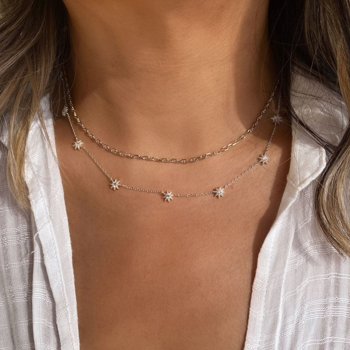 Sterling silver white zirconia starburst necklace layered over a chain, shown on a model's neckline