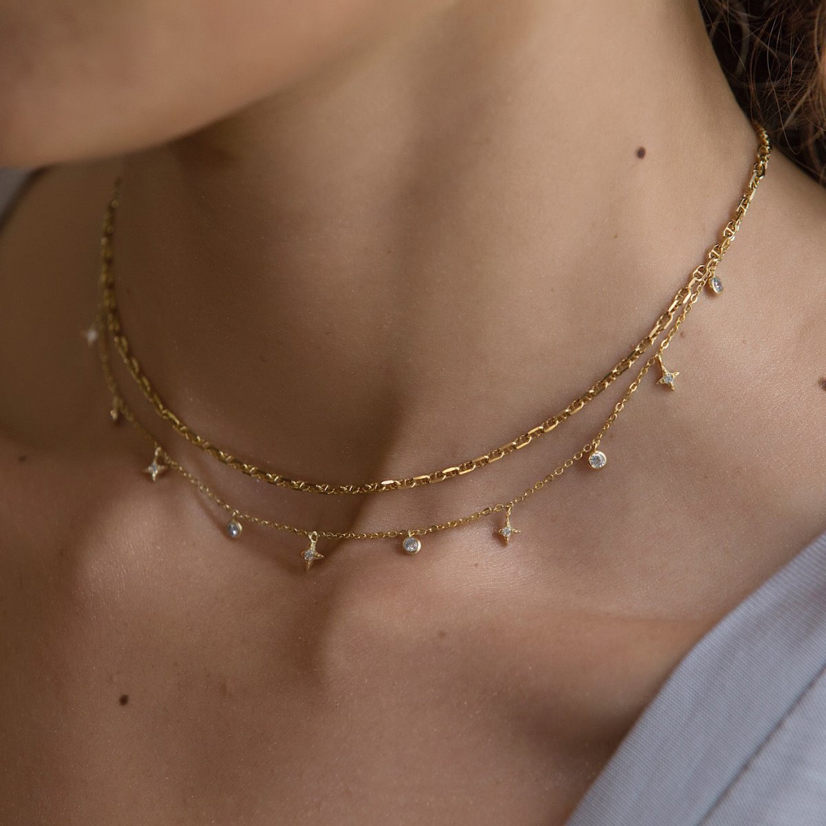 Gold vermeil star dangle necklace with white zirconia star charms, close-up on a model's neckline
