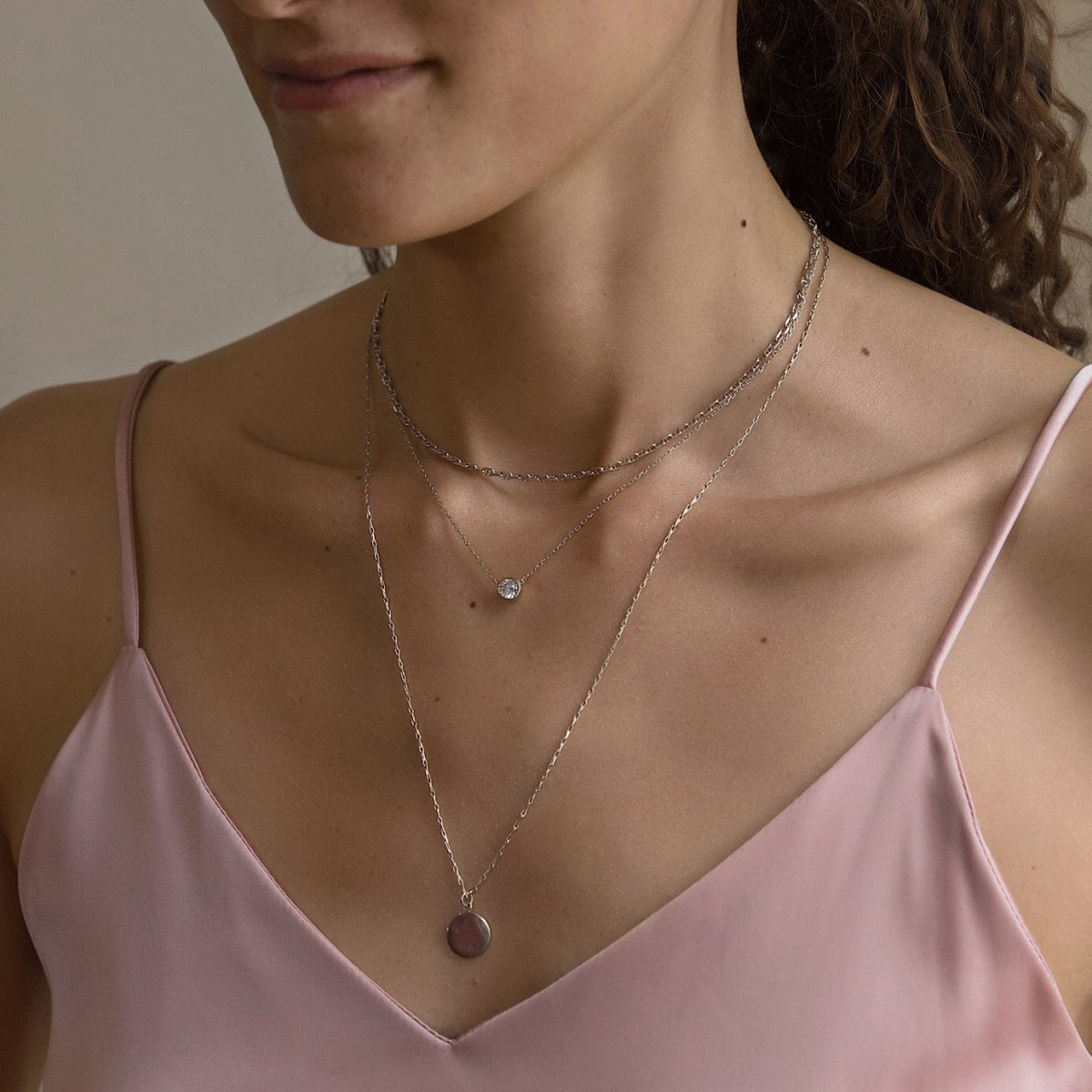 Sterling silver layered chain necklaces with a small round pendant, shown on a model's neckline