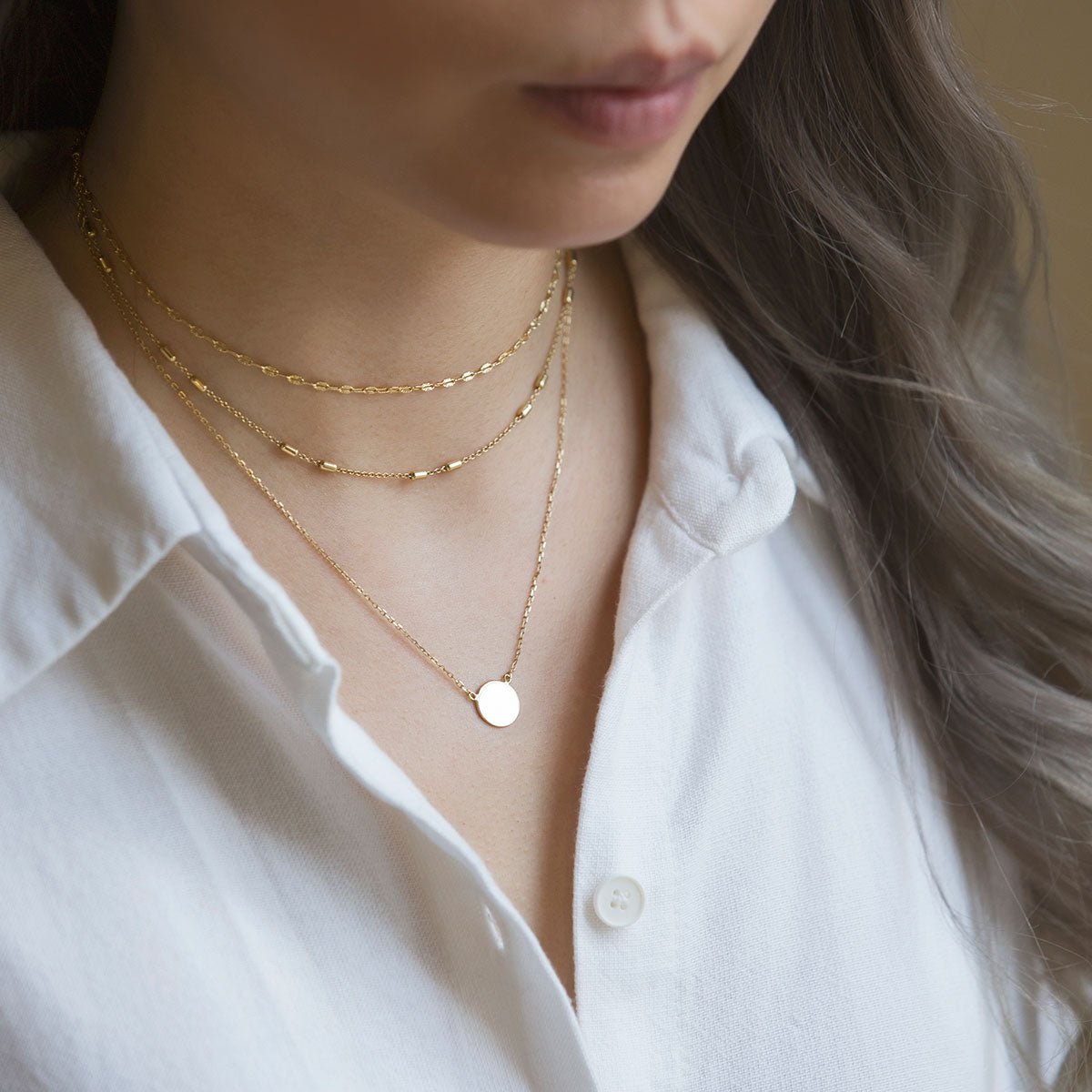 Gold three-strand layered necklace with a small round disc pendant, shown on a model's neckline