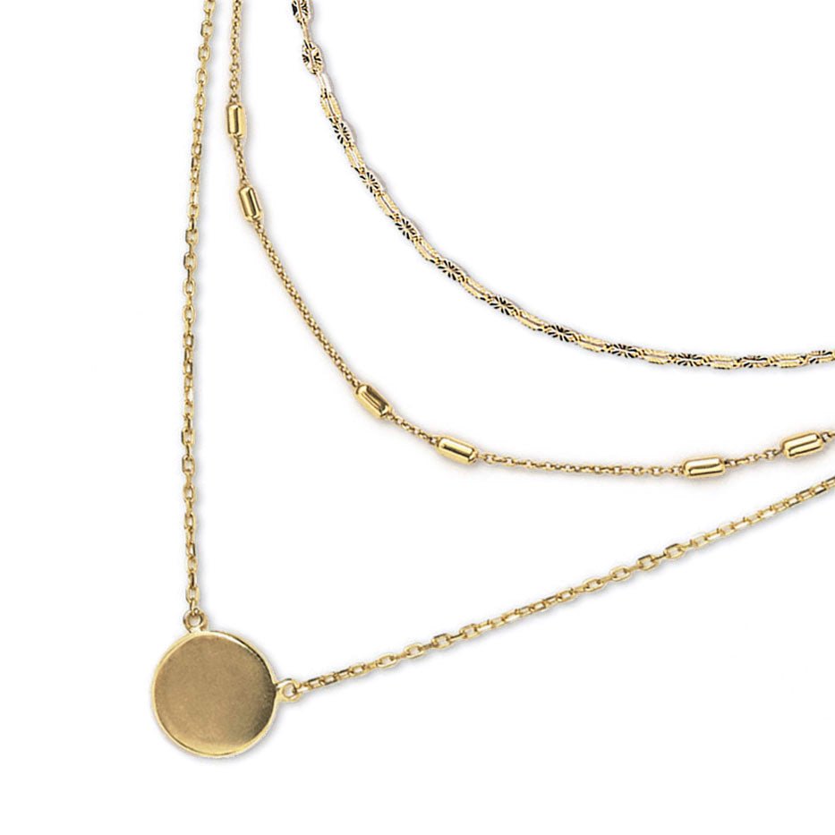Gold triple-layered necklace with mixed chains and a disc pendant, on a white background