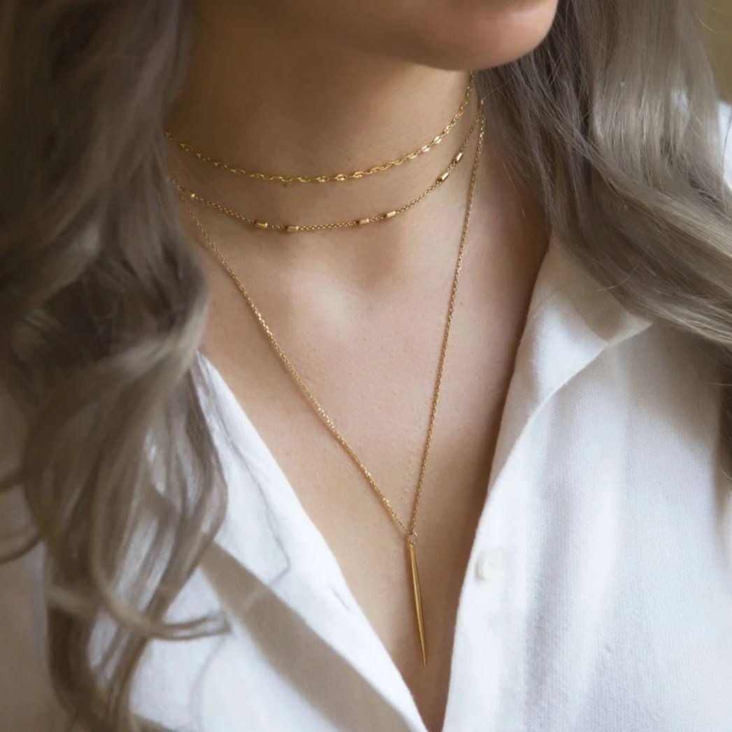 Gold vermeil layered necklace with a slim needle bar drop, shown on a model in a white shirt