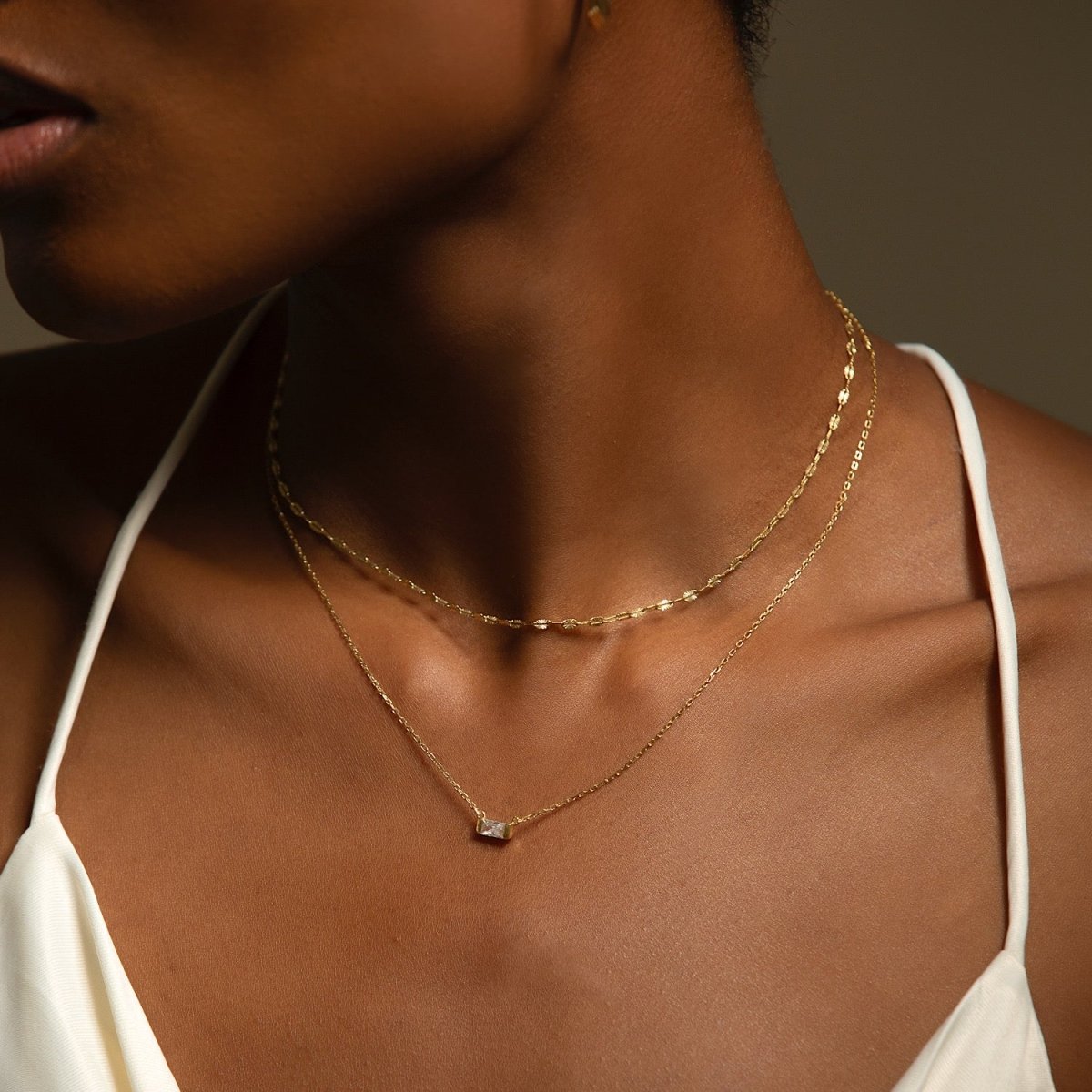 Gold vermeil baguette zirconia necklace with a single clear stone, shown on a model's neckline