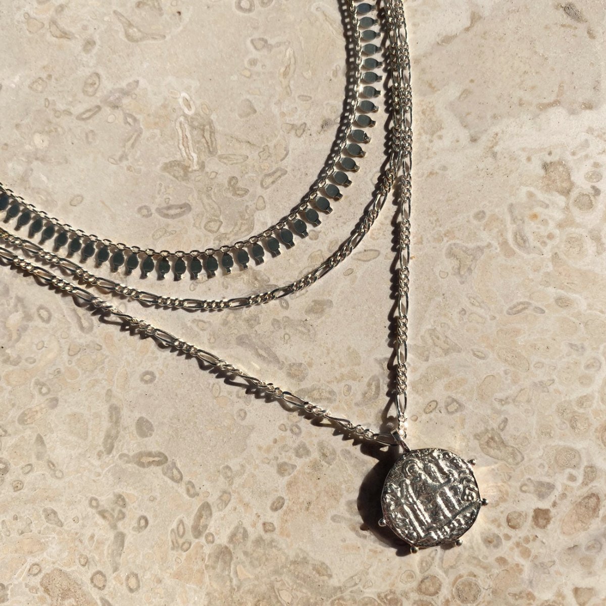 Sterling silver layered necklaces with a coin pendant, laid on white marble