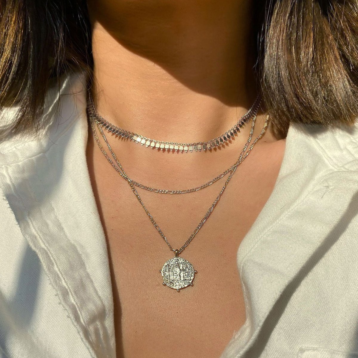 Sterling silver coin pendant and chain layered necklaces shown stacked on a model's neckline