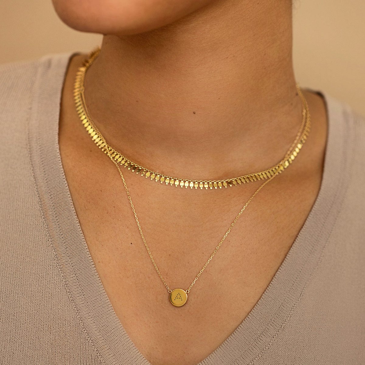 Gold vermeil disc necklace engraved with an initial, layered with a wide chain on a model's neckline
