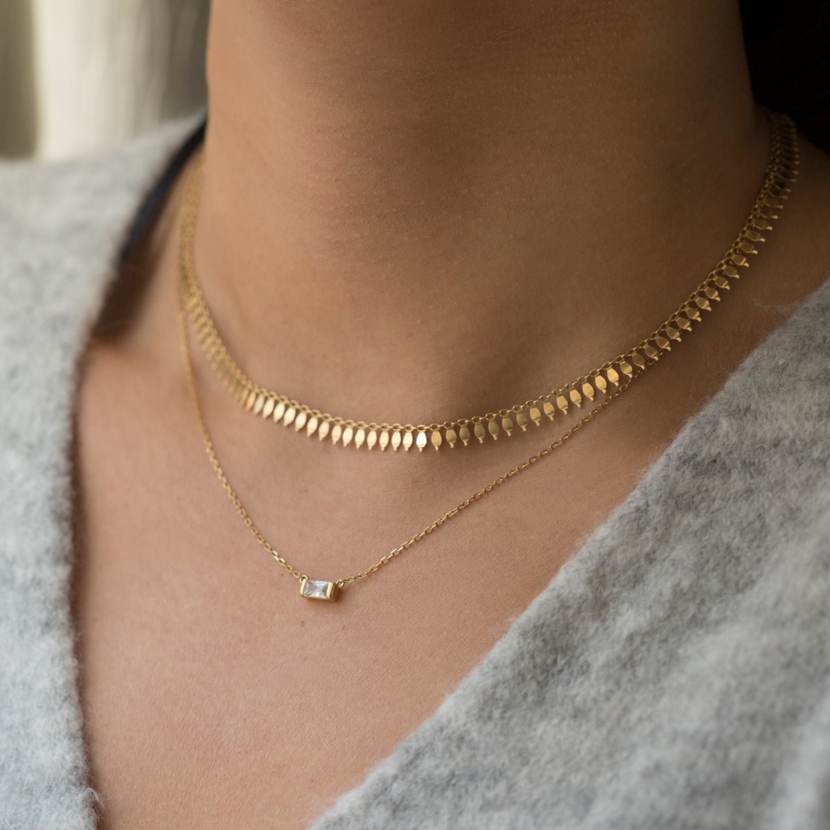 Gold vermeil layered necklaces with a clear baguette pendant, shown on a model's neckline