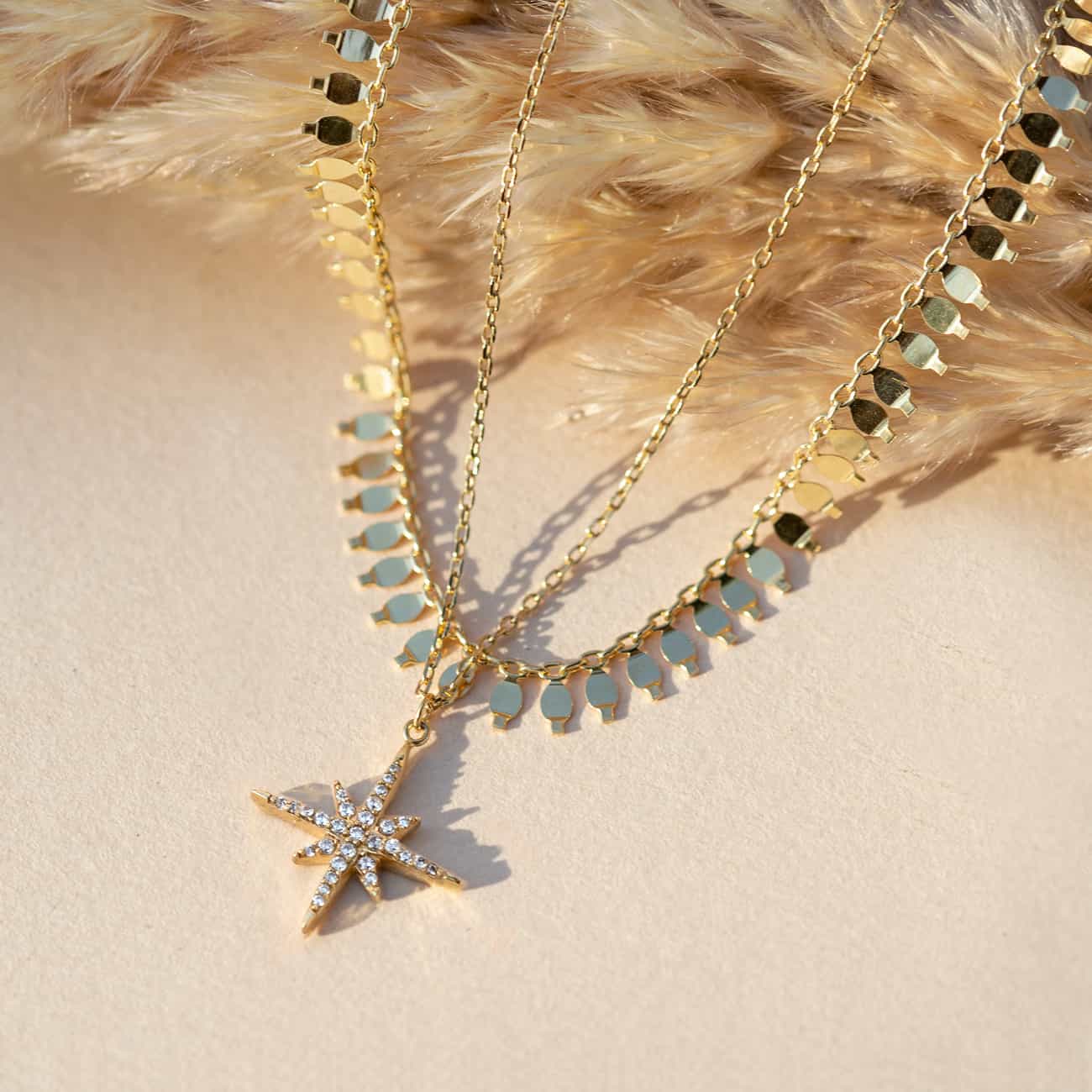 Gold vermeil layered duo with a clear-stone starburst pendant and disc fringe chain, on a cream background