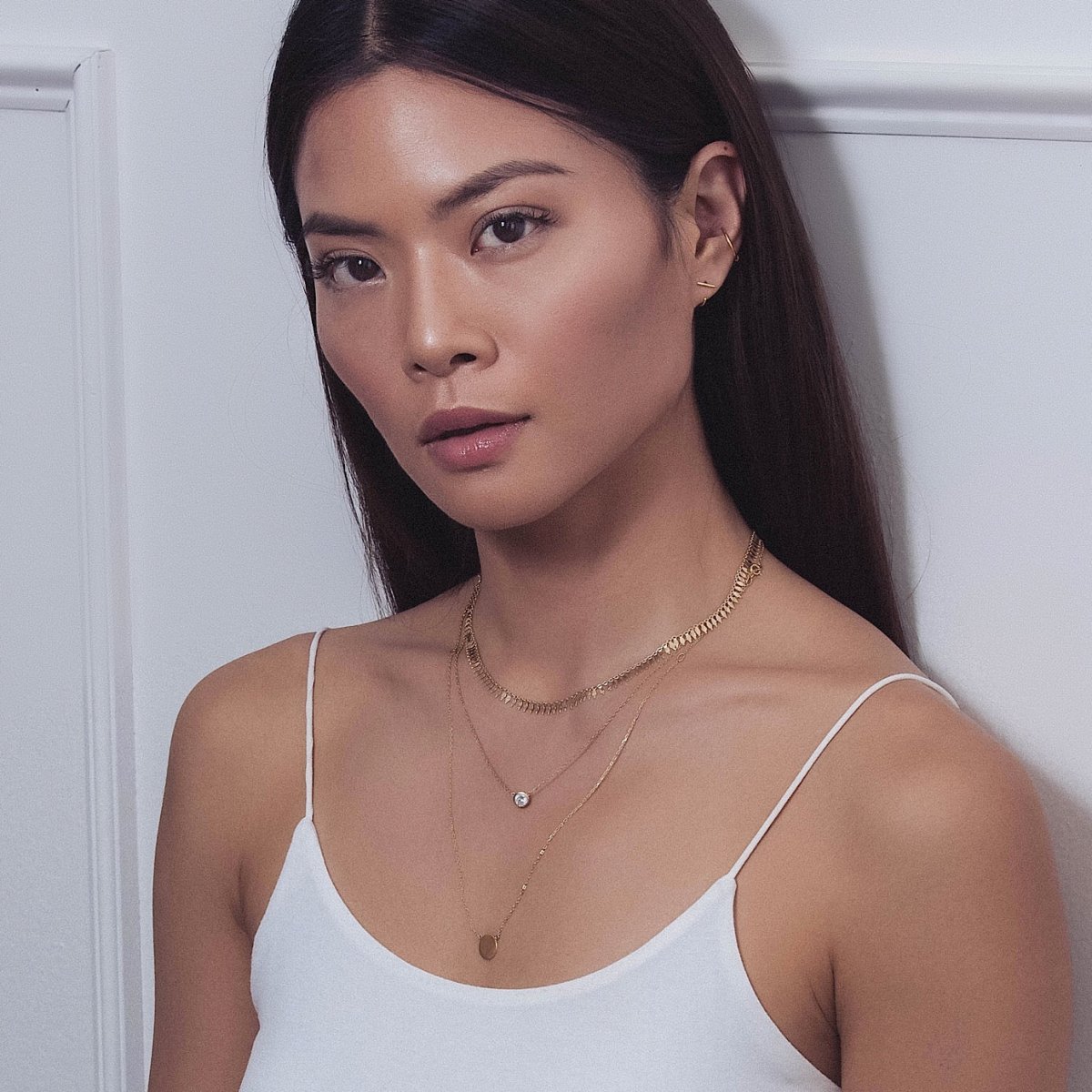 Gold vermeil layered necklaces with a clear stone and small disc coin, shown on a model's neckline