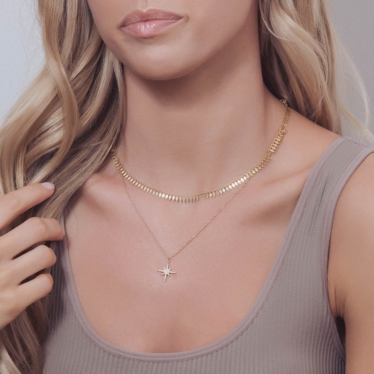 Gold vermeil starburst pendant with clear stones, layered over a tank top on a model's neckline