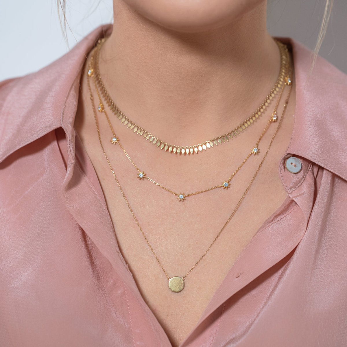 Gold vermeil layered trio with a starburst station chain and disc pendant, shown on a model's neckline
