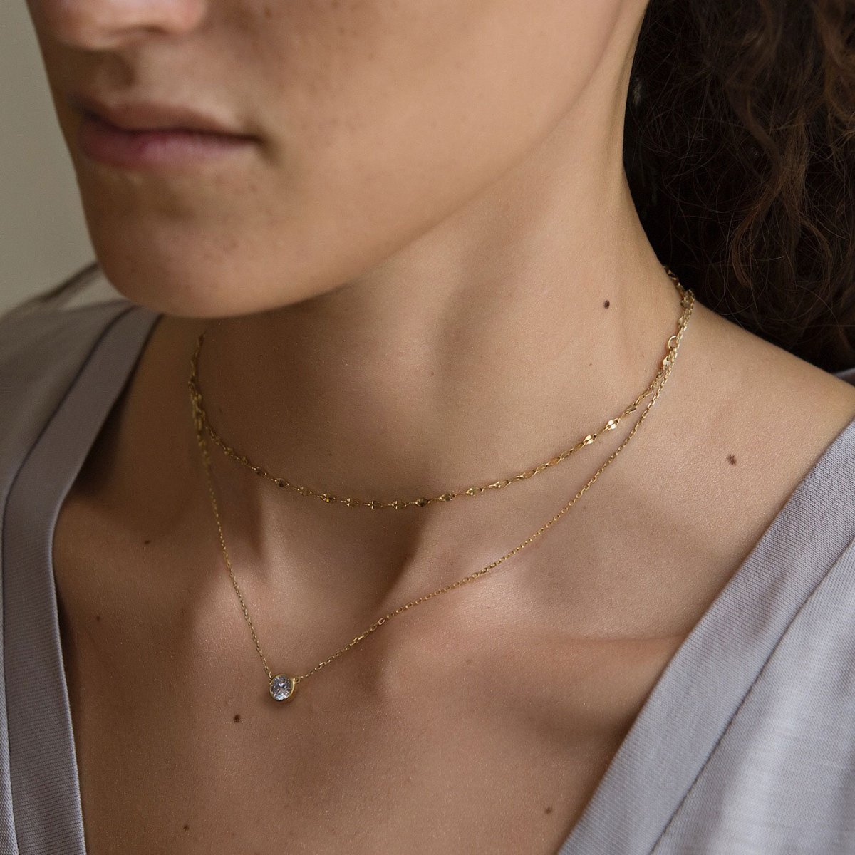Gold vermeil layered necklace duo with a bezel-set round clear solitaire stone, shown on a model's neckline
