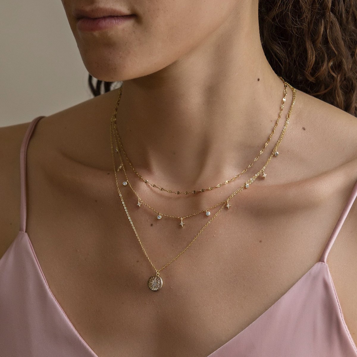 Gold vermeil layered duo of a starburst disc and a star station chain, shown on a model's neckline