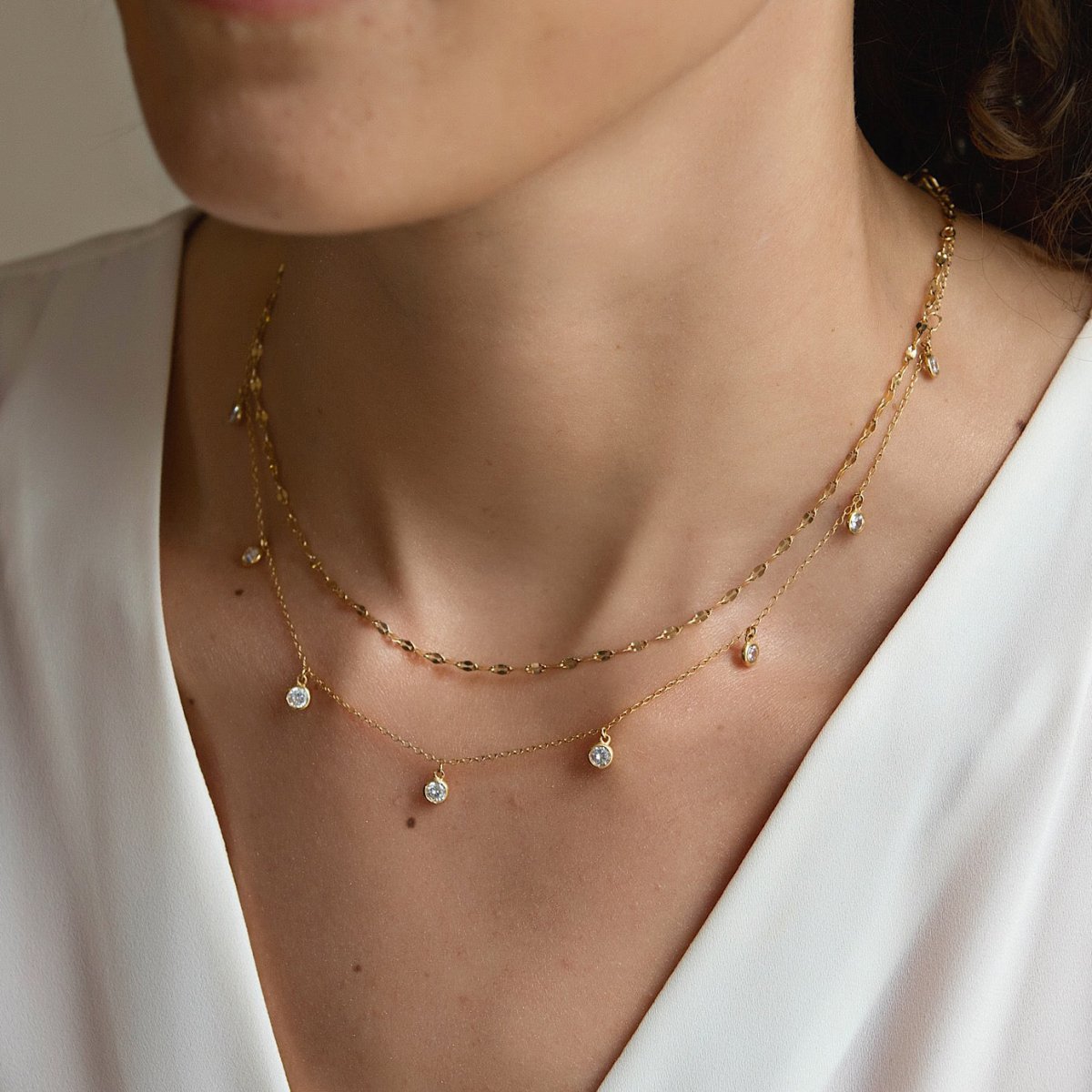 Gold vermeil layered necklace duo with dangling clear stones, shown on a model's neckline