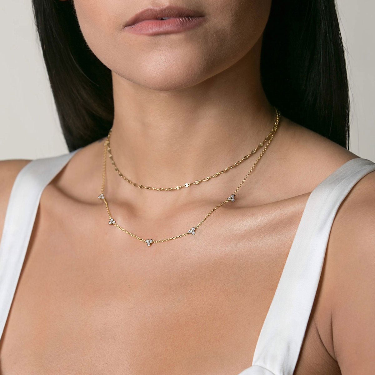 Gold vermeil necklace with three clear-stone clover clusters, shown layered on a model's neckline