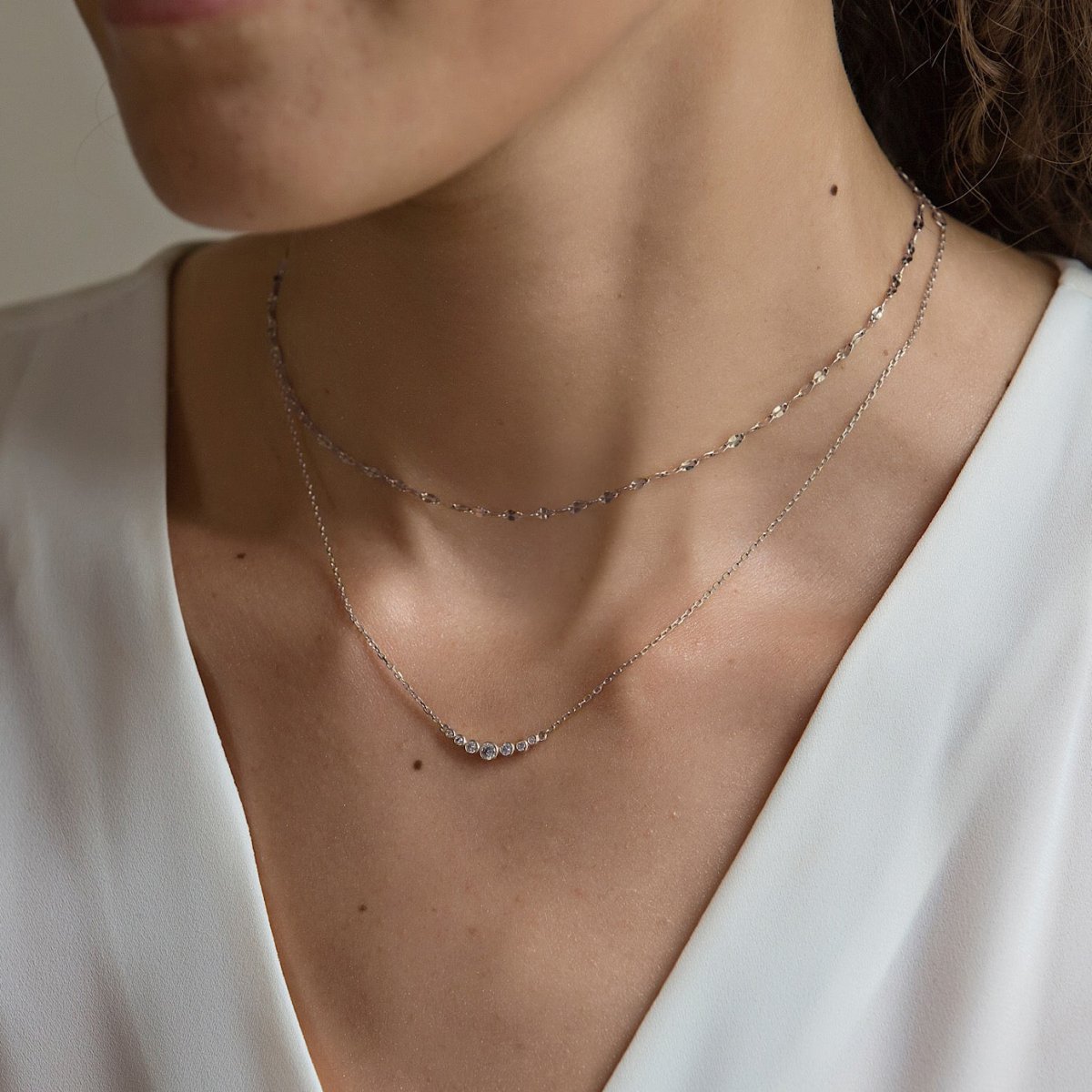 Sterling silver curved bar necklace with clear stones, shown layered on a model's neckline