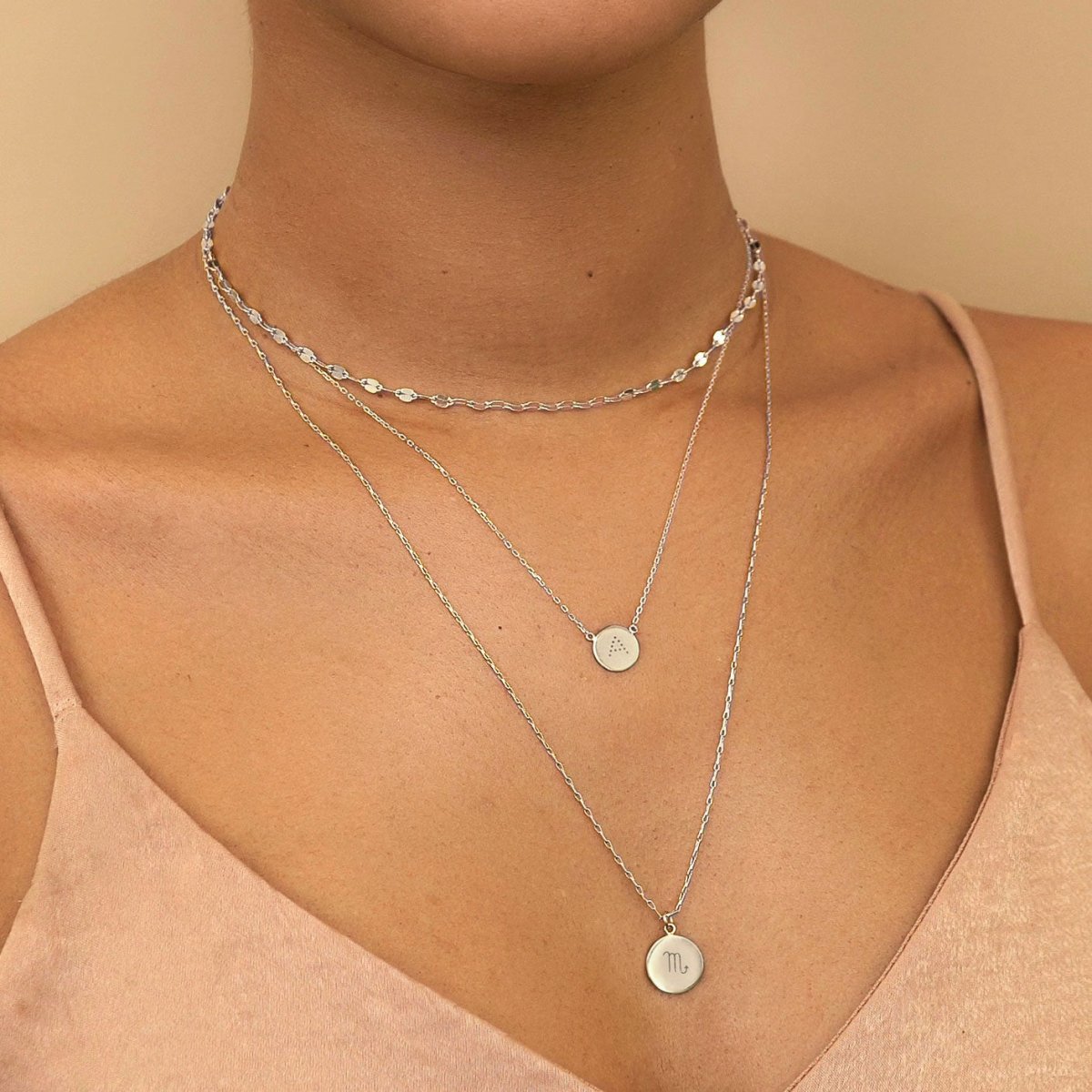 Sterling silver zodiac disc necklaces with engraved symbols, shown layered on a model's neckline