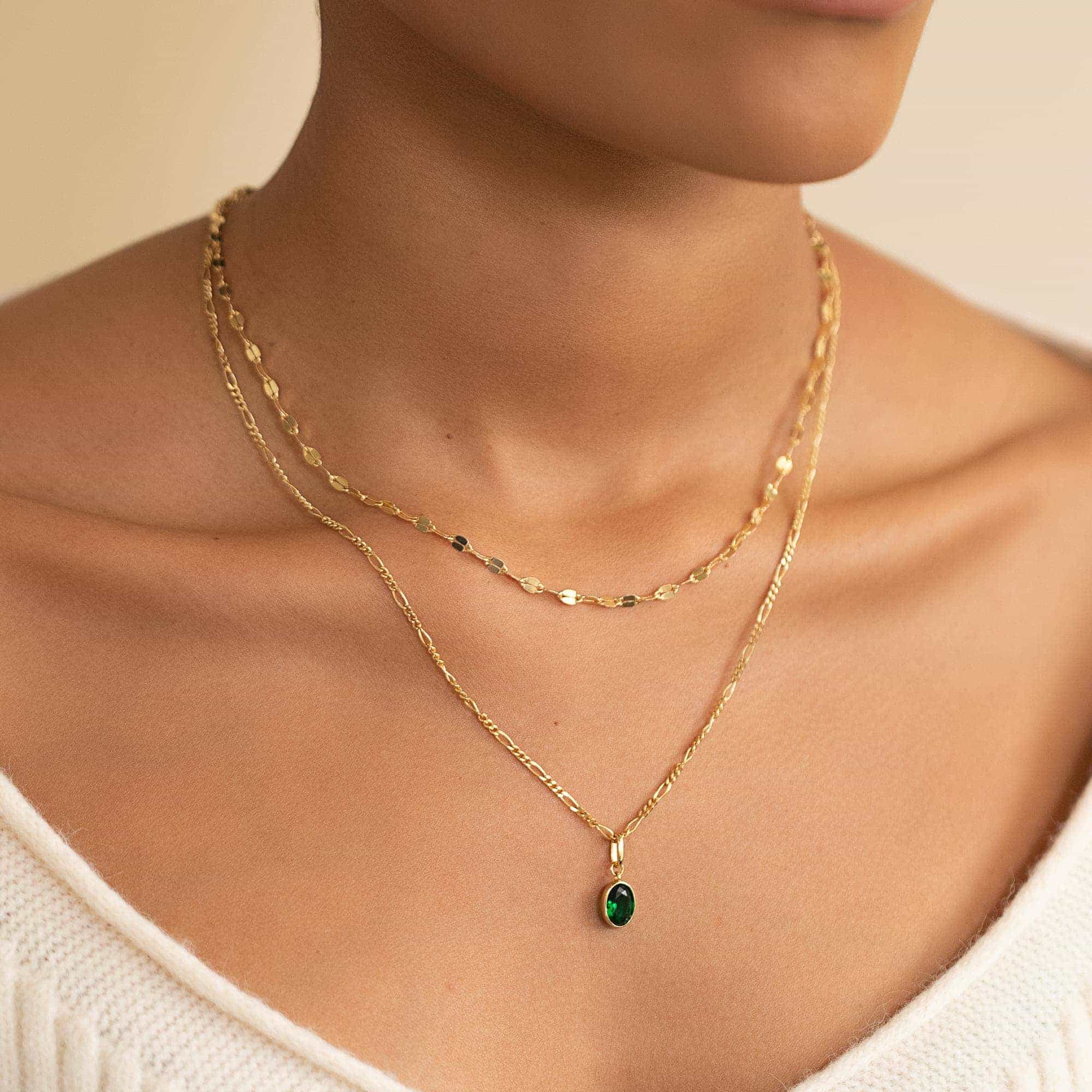 Two gold chains layered on a model's neckline with an oval green-stone pendant