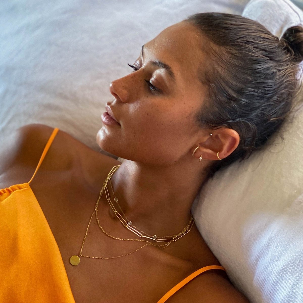Gold vermeil disc pendant necklace shown on a reclining model with layered paperclip chains