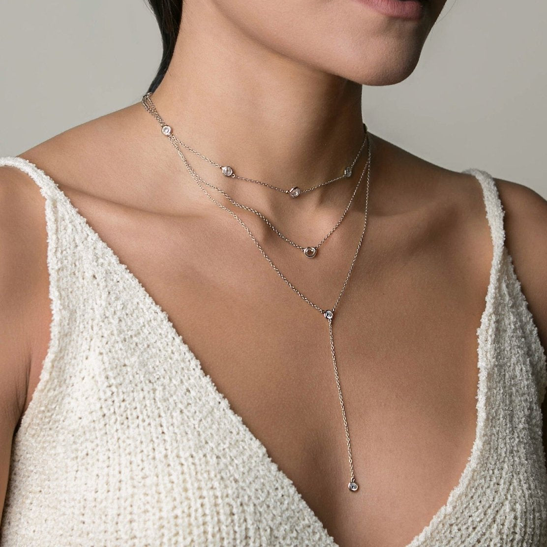 Sterling silver zirconia lariat necklace layered with shorter chains, shown on a model's neckline