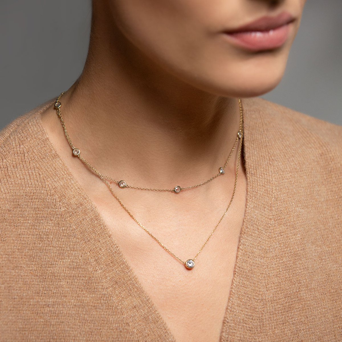 Gold vermeil layered station chain and clear solitaire pendant duo, shown on a model's neckline