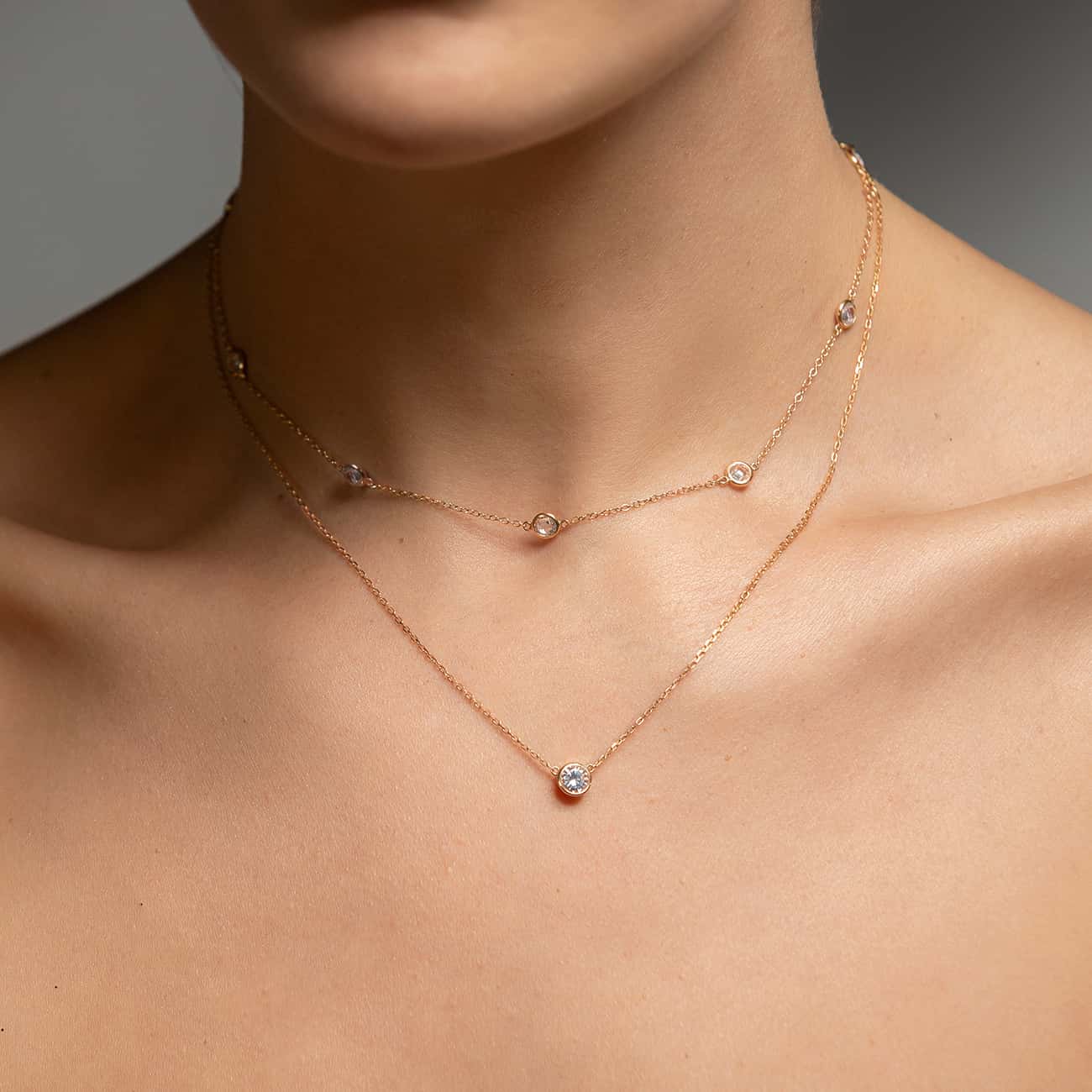 Rose gold layered station and solitaire necklaces with clear stones, shown on a model's neckline