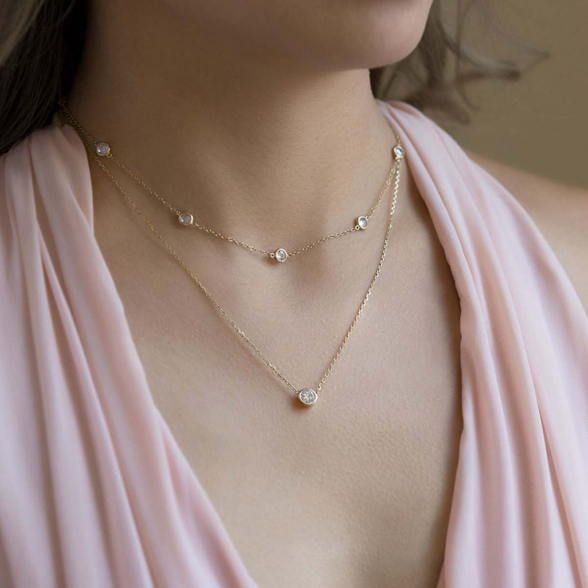 Gold vermeil layered station chain and clear solitaire pendant duo, shown on a model's neckline