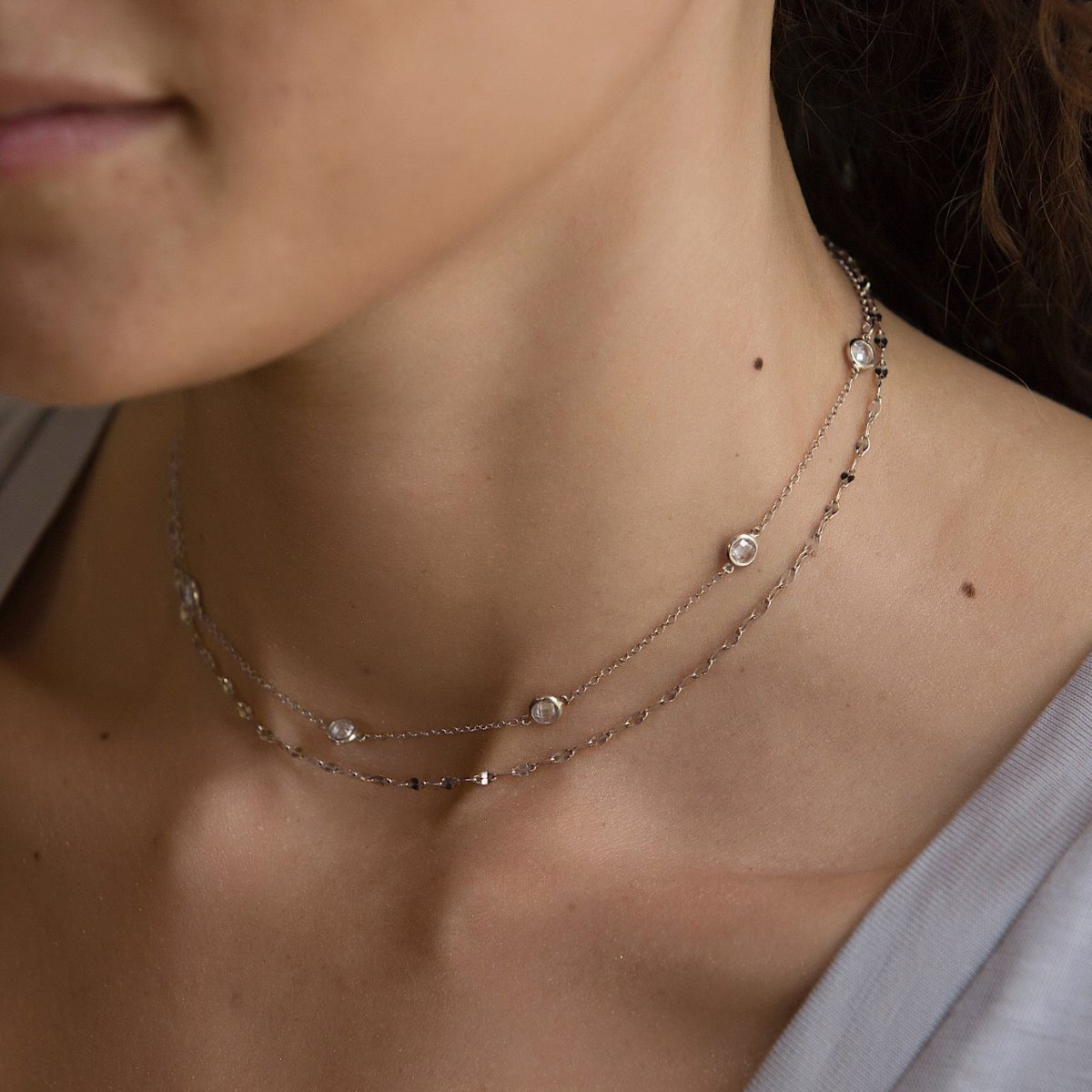 Sterling silver layered station necklace with clear stones, shown on a model's neckline
