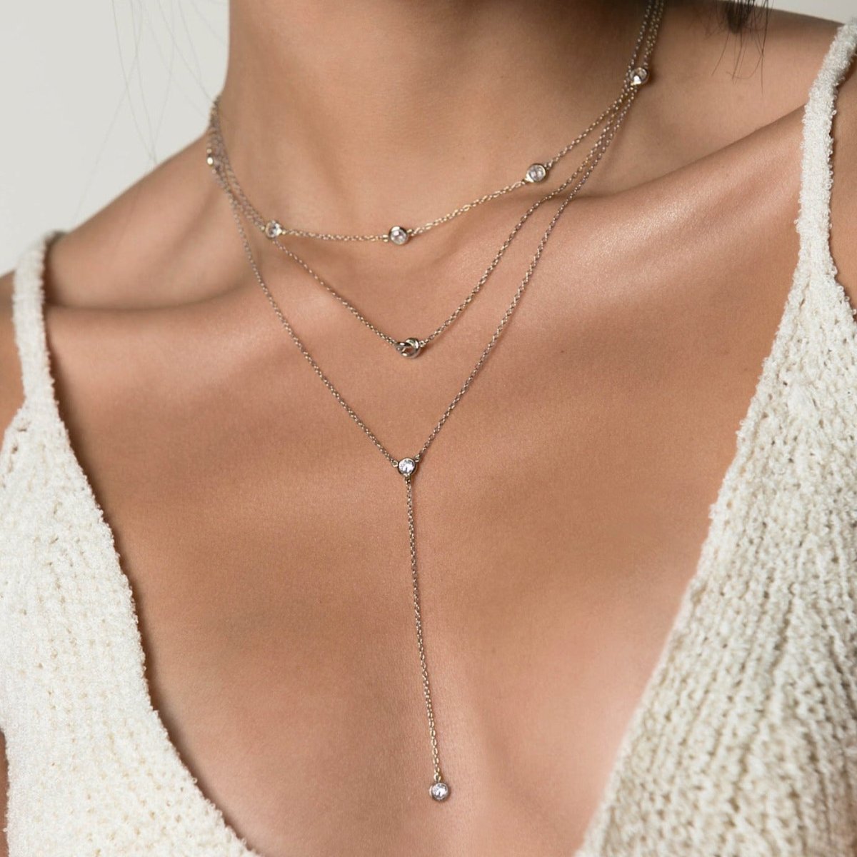 Sterling silver love knot necklace layered with other chains, shown on a model's neckline