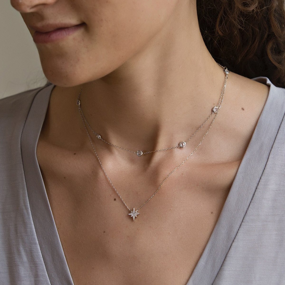 Sterling silver starburst pendant necklace with a white zirconia star, shown close on a model's neckline