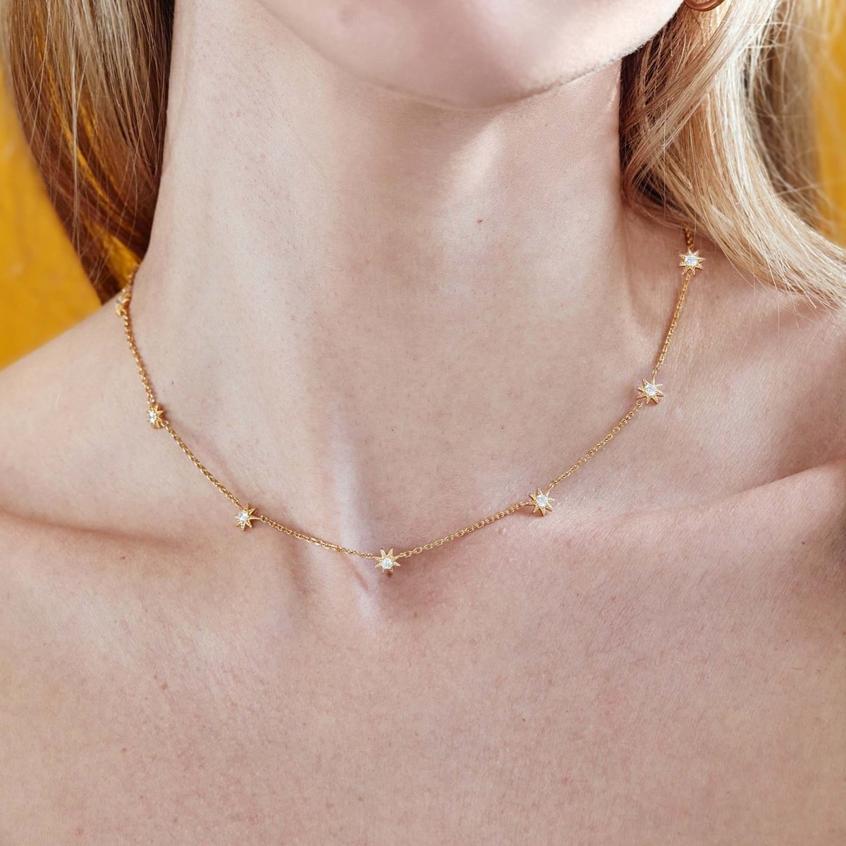 Gold vermeil starburst station necklace with white zirconia stars, shown on a model's neckline