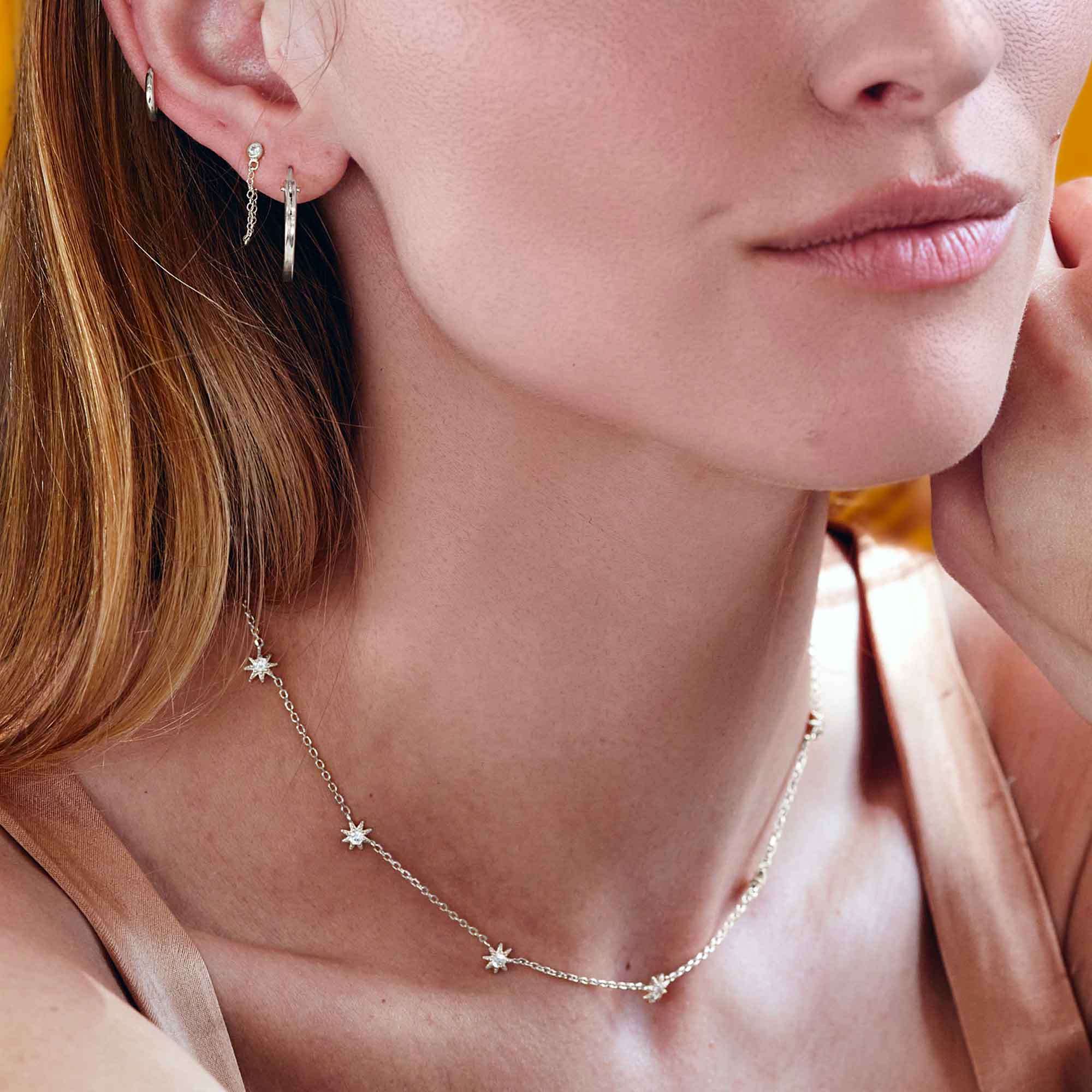 Sterling silver starburst necklace with white zirconia stars, shown on a model with matching hoops