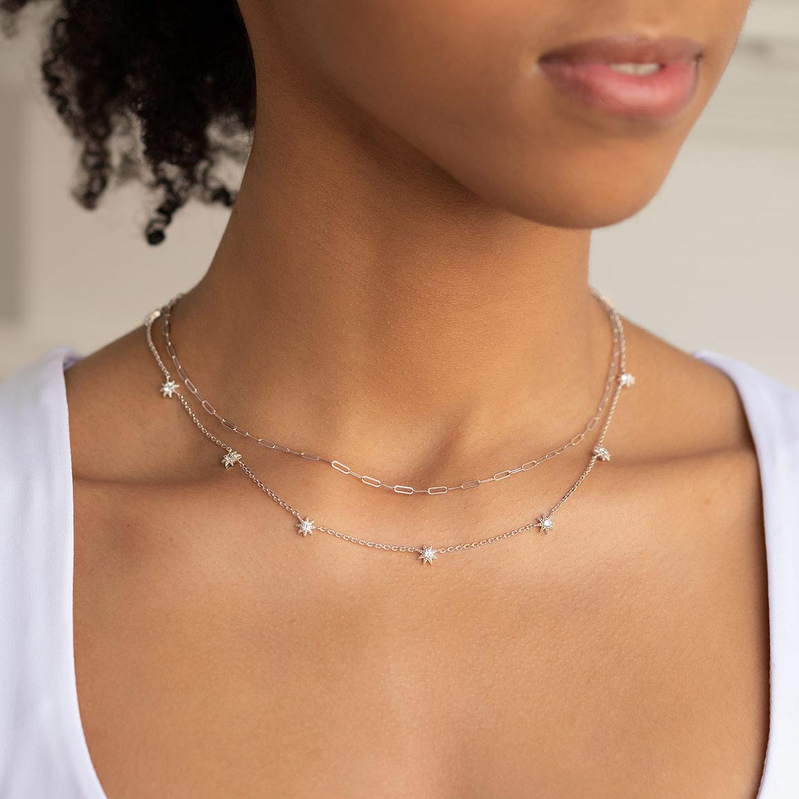 Sterling silver white zirconia starburst necklace layered with a chain, shown on a model's neckline