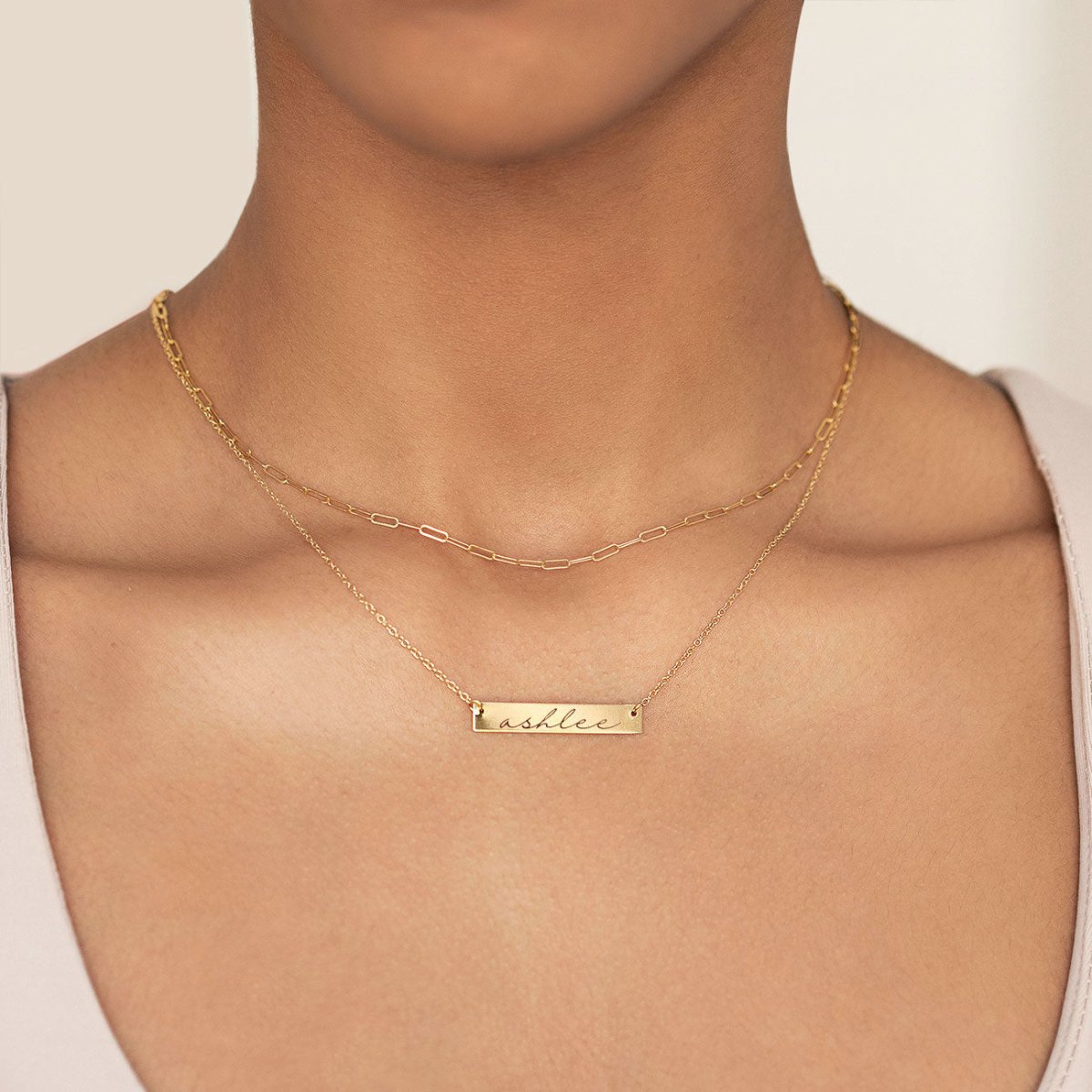 Gold vermeil name bar necklace engraved with a name, layered under a paperclip chain on a model