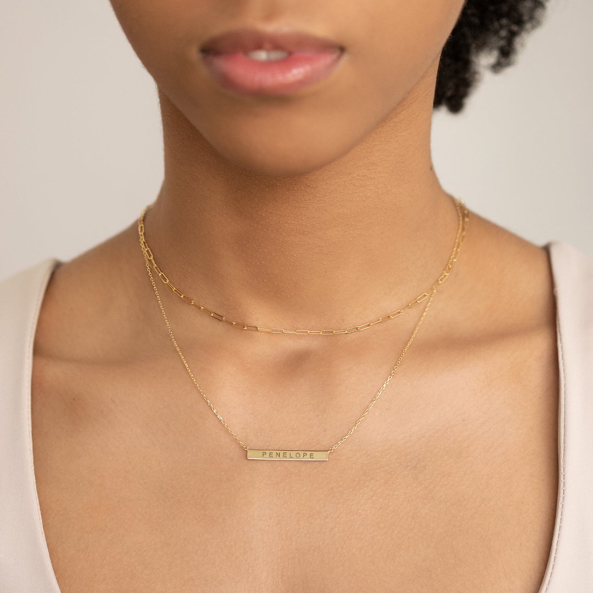 Gold vermeil bar necklace engraved with a name, layered with a chain on a model's neckline