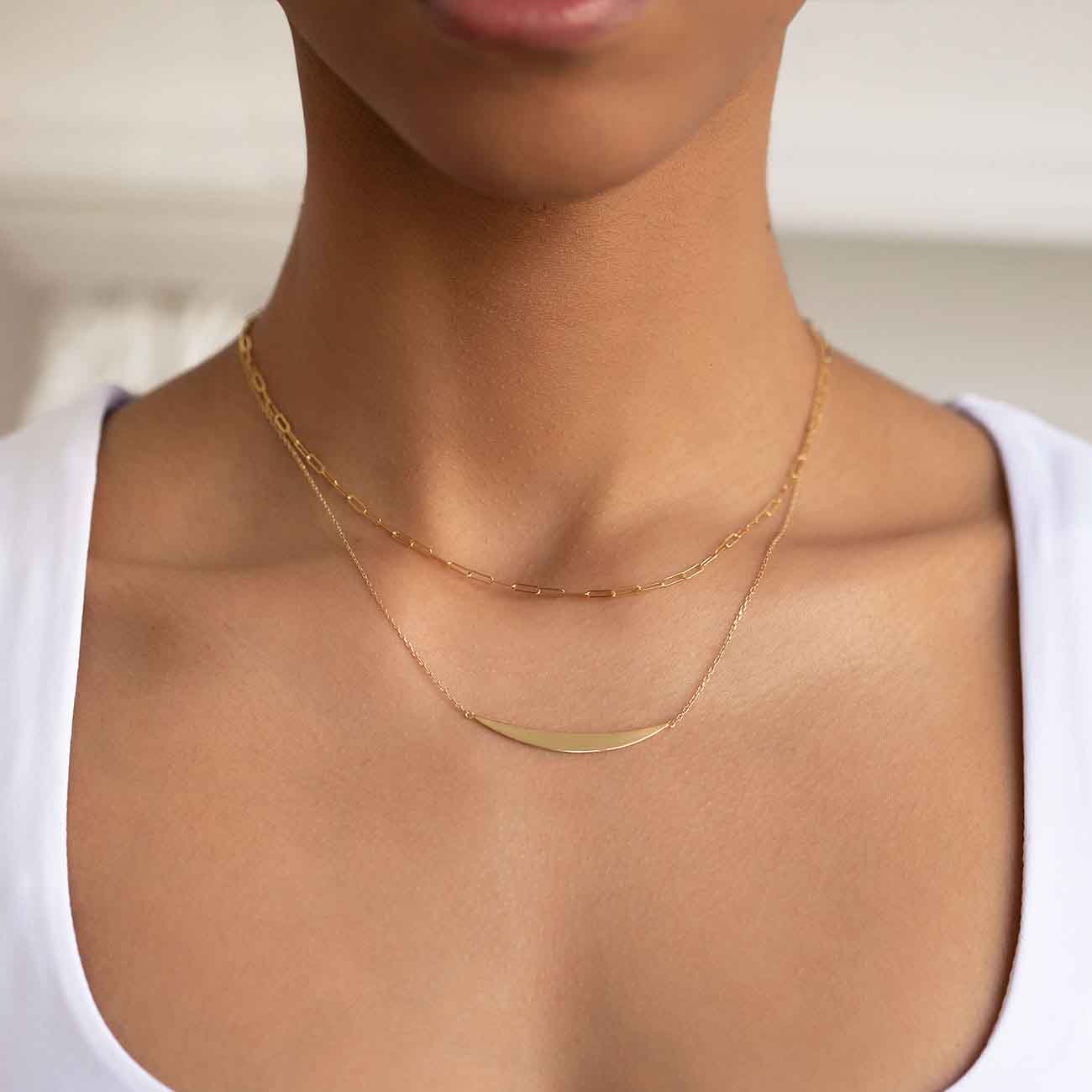 Gold vermeil crescent bar necklace shown on a model's neckline, layered with a paperclip chain
