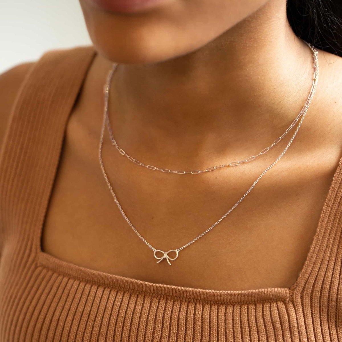 Sterling silver paperclip chain necklace layered with a finer bow chain on a model's neckline