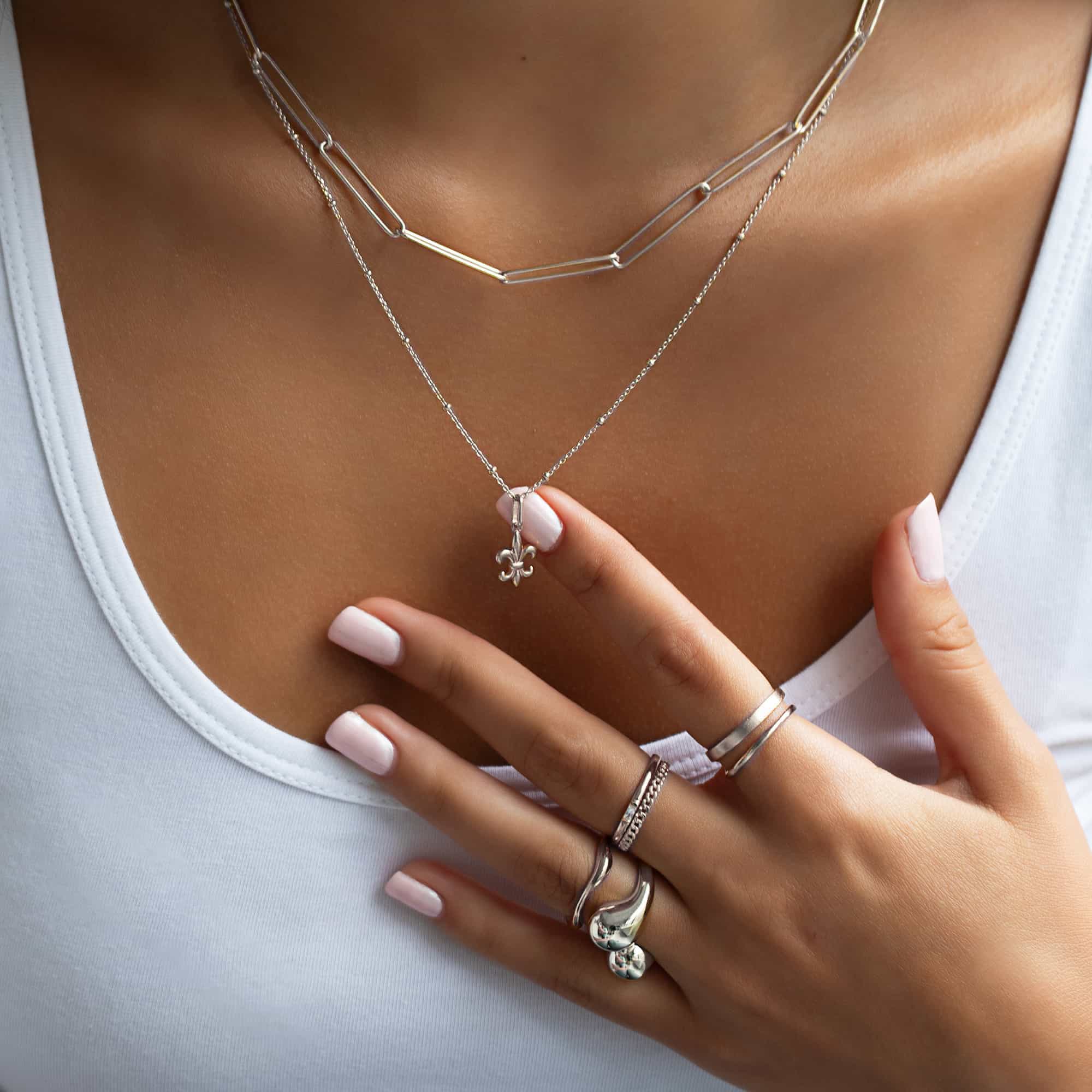 Sterling silver fleur-de-lis pendant shown held on a model's beaded chain necklace