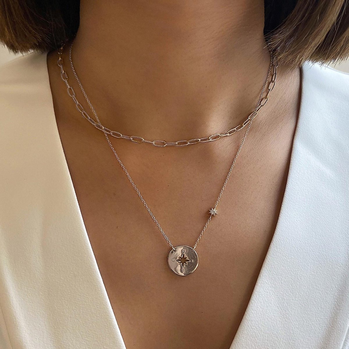 Sterling silver compass disc necklace with a star station, layered on a model's neckline