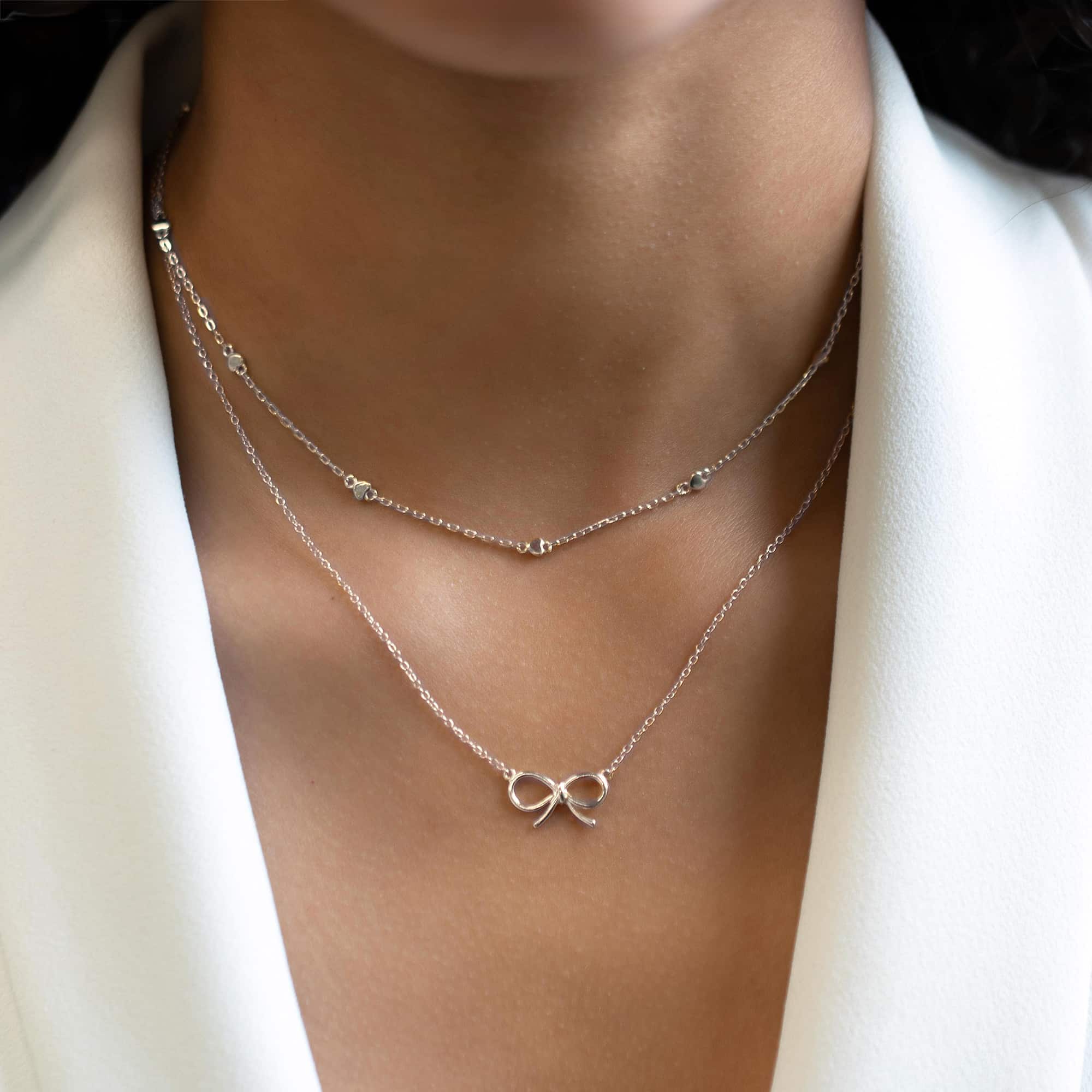 Layered silver necklaces, including a beaded chain and a bow pendant, on a model's neckline