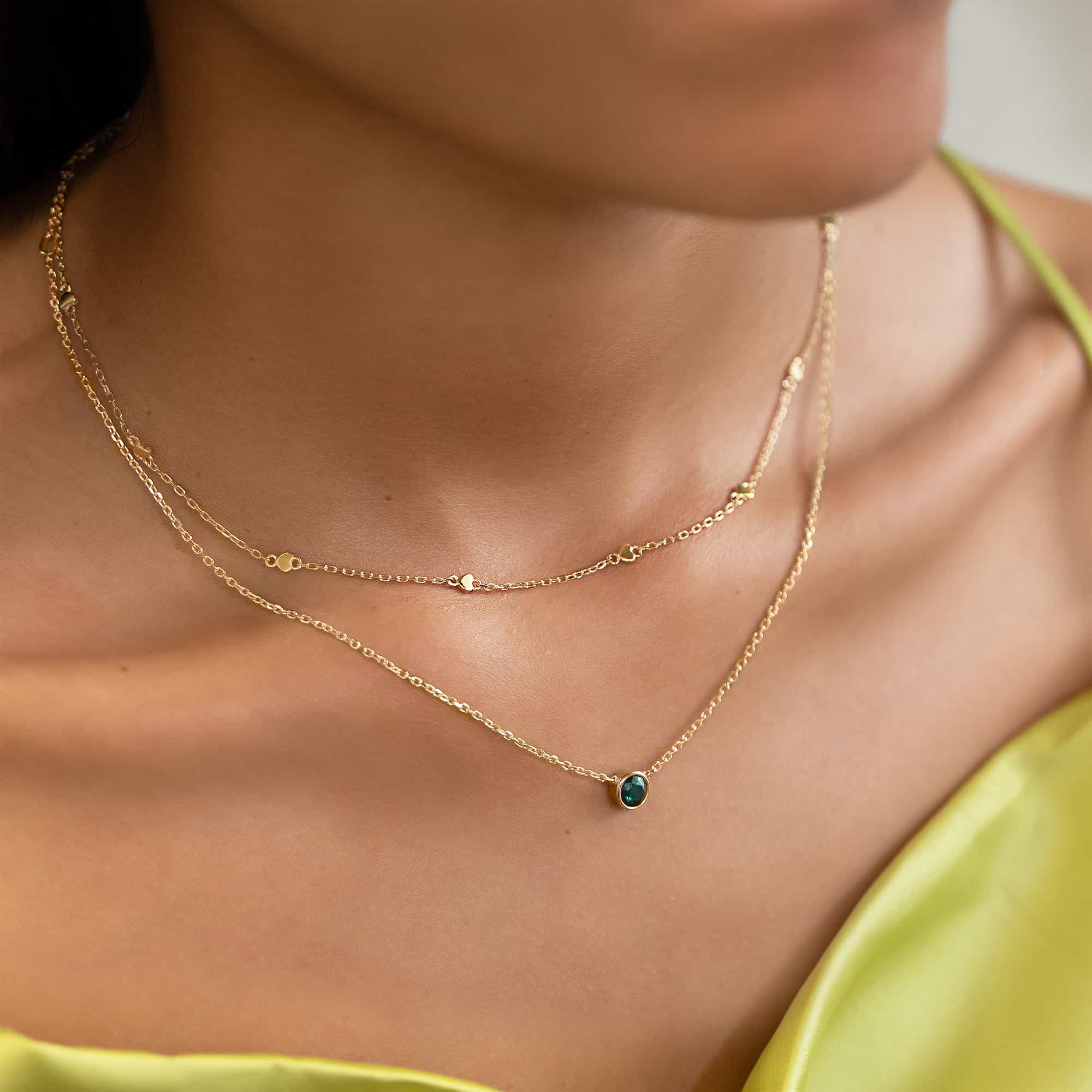 Gold heart-station chain layered with a green-stone solitaire necklace on a model's neckline
