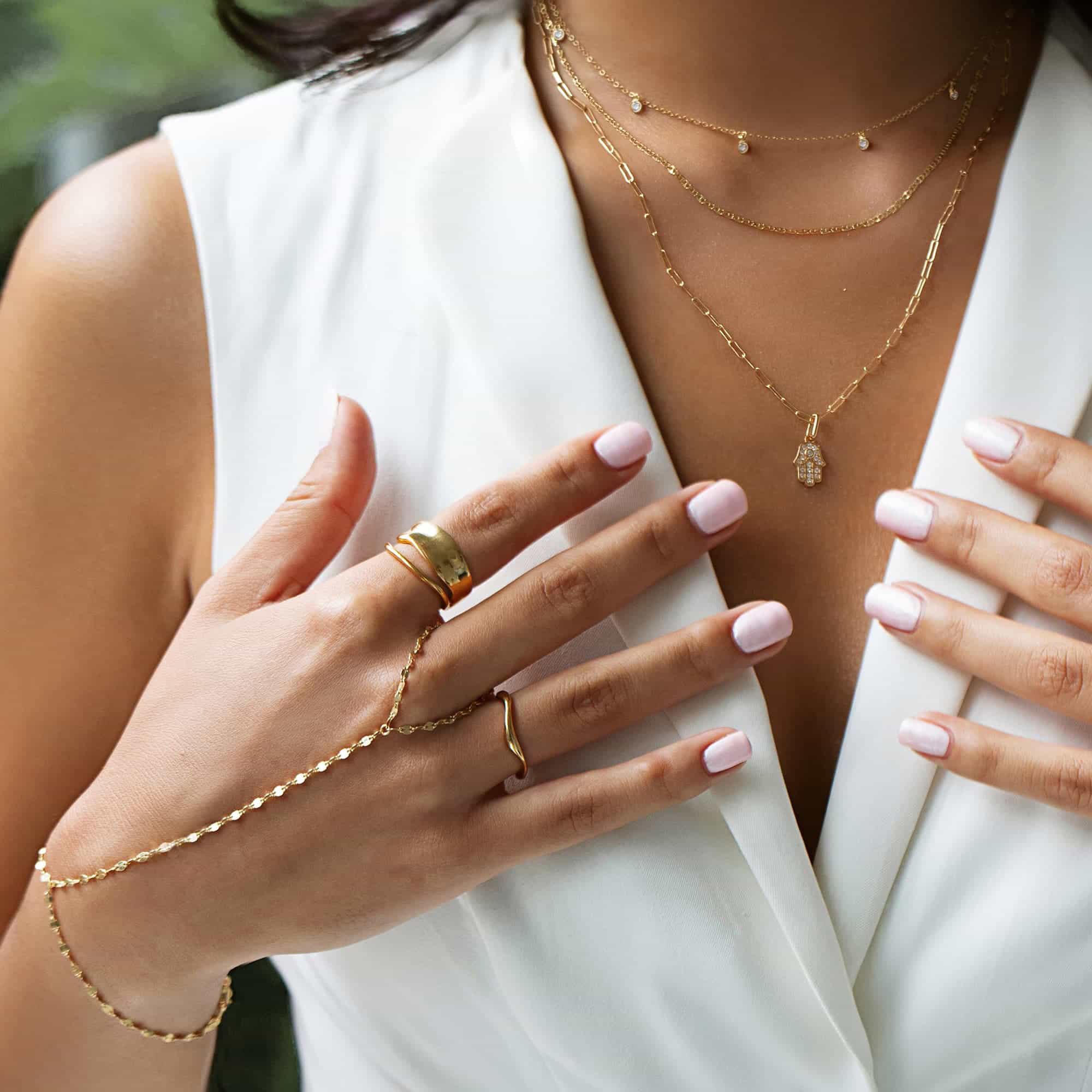 Gold vermeil faceted hand chain on a model's hand with layered necklaces and rings