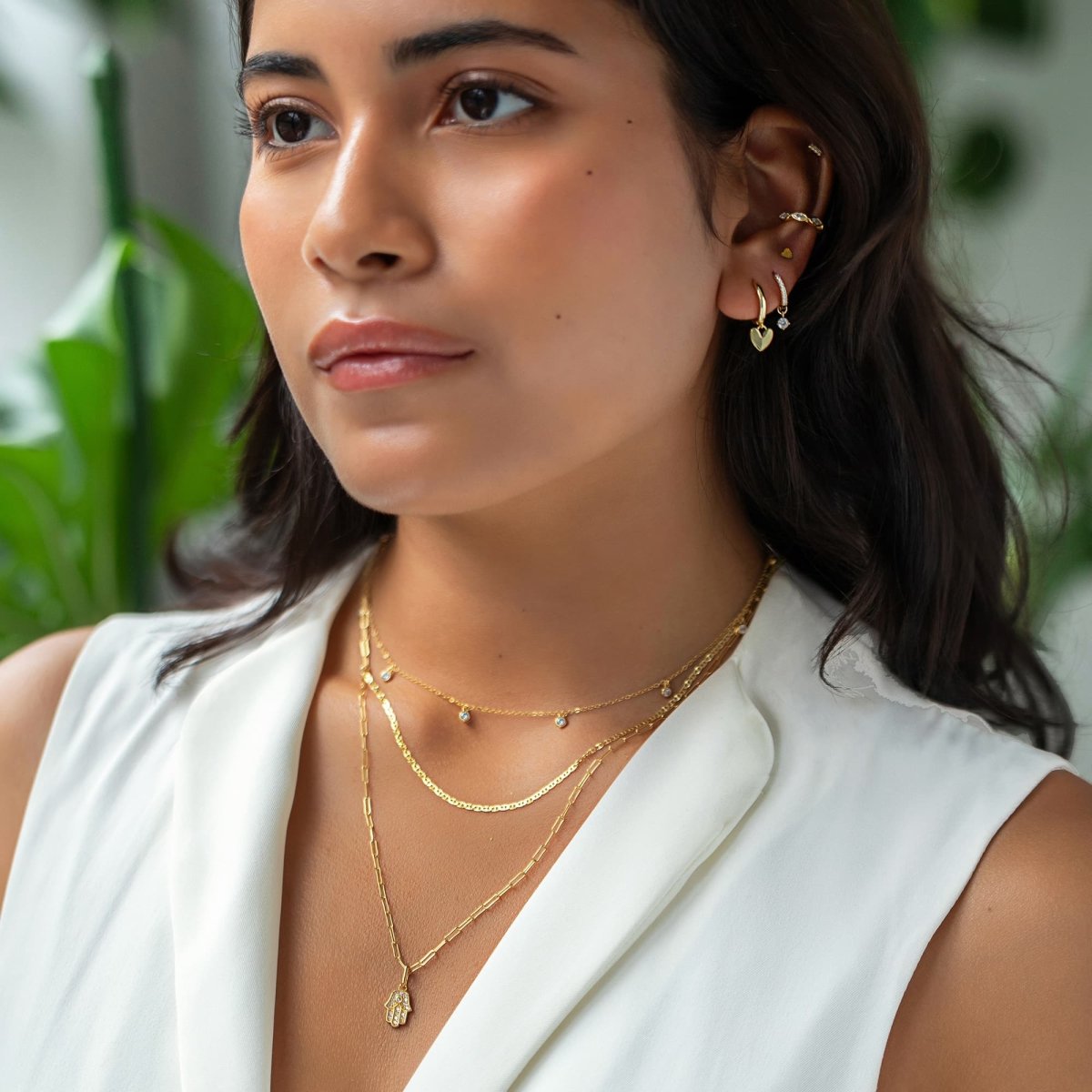 Gold vermeil heart-charm huggie shown in a layered ear and necklace look on a model