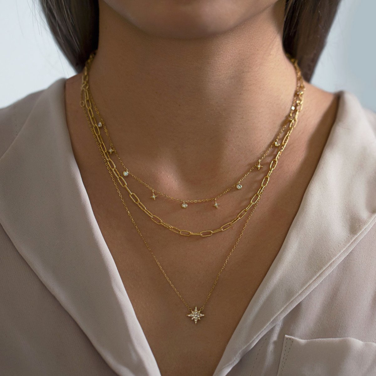 Gold vermeil starburst layered chain trio with clear crystal accents, shown on a model's neckline