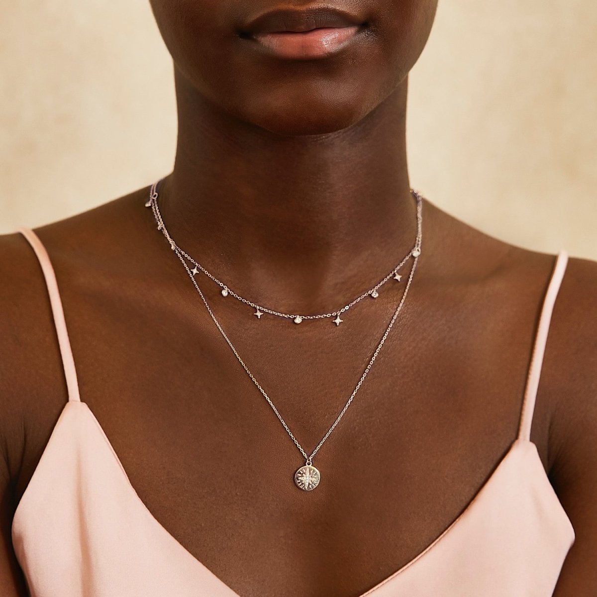 Sterling silver star disc necklace with a starburst pendant, shown on a model's neckline