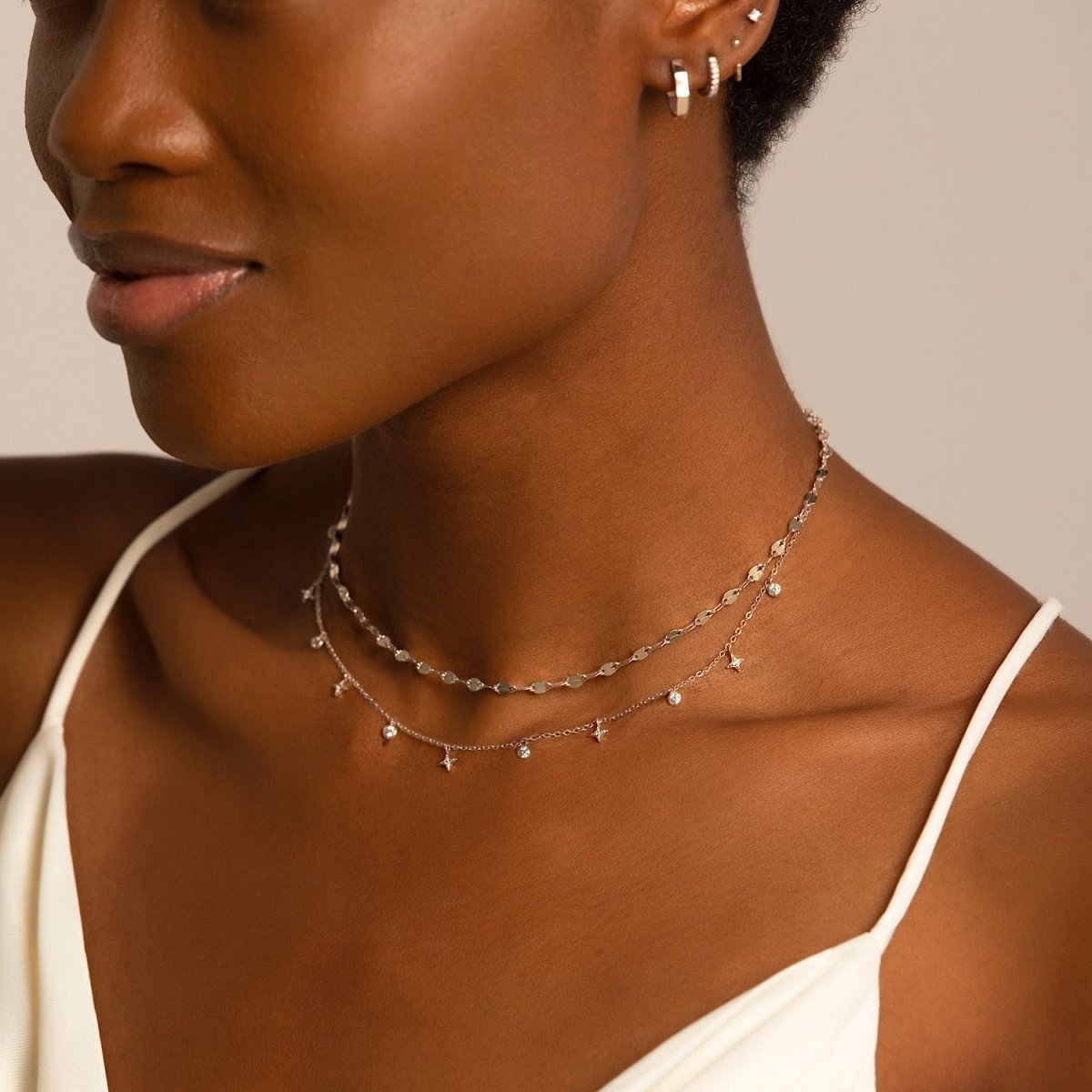 Sterling silver mirror-link chain necklace layered with a star-charm chain, shown on a model's neckline